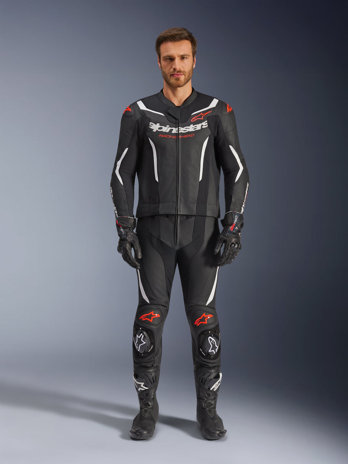 Combinaison en cuir 2 pièces Alpinestars GP Force V2, combinaison de course moto, noir, blanc et rouge fluo, portée par un mannequin avec gants et bottes noirs assortis, dotée de panneaux en cuir perforé, d'accents blanc et rouge fluo, et d'un design aérodynamique élégant pour la piste et la conduite sportive