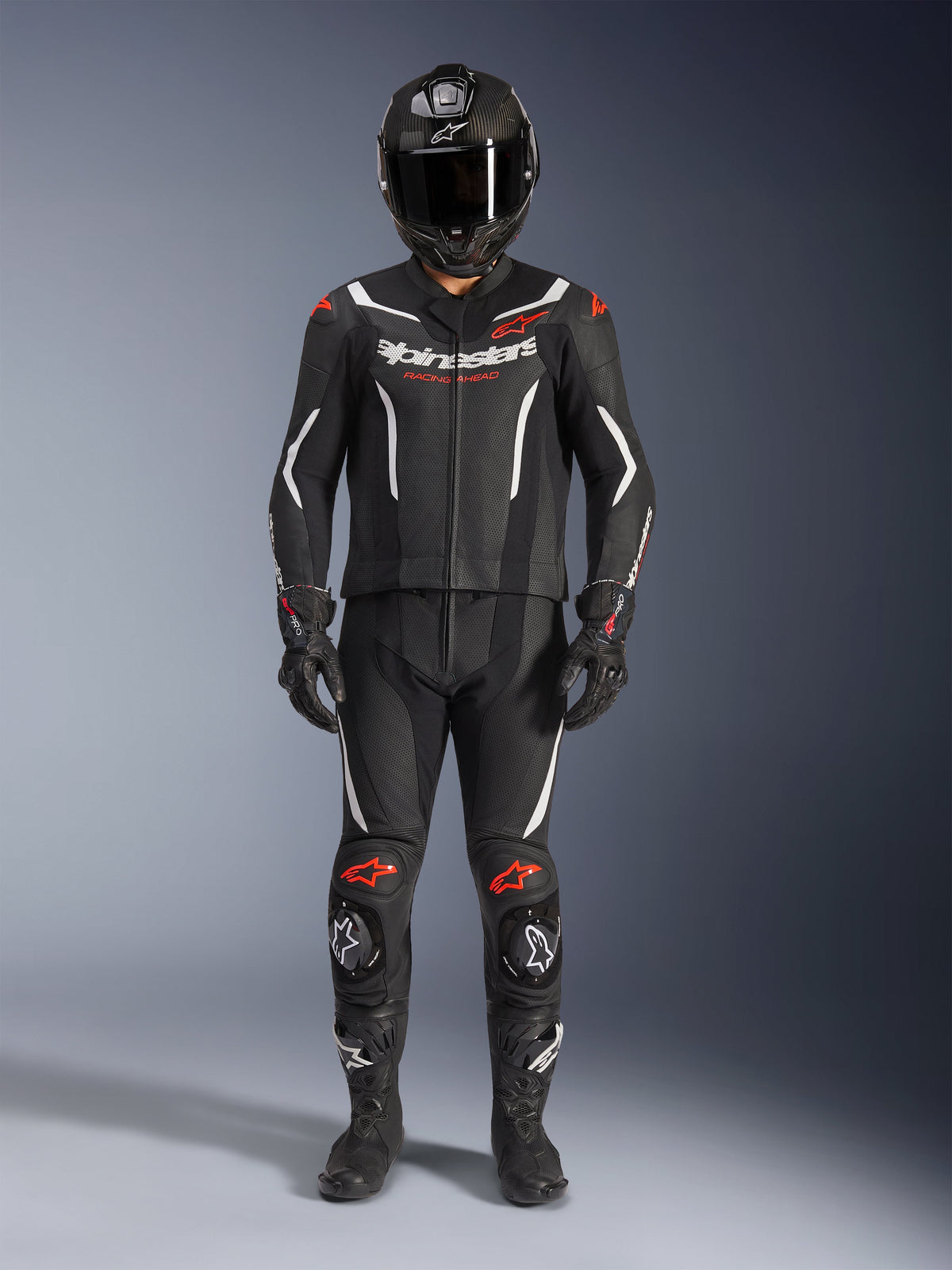 Combinaison en cuir 2 pièces Alpinestars GP Force V2, combinaison de course moto, noir, blanc et rouge fluo, avec logo Alpinestars blanc sur la poitrine et détails rouges aux épaules et aux genoux, portée avec un casque intégral noir, des gants noirs et des bottes noires pour un ensemble complet d'équipement de performance
