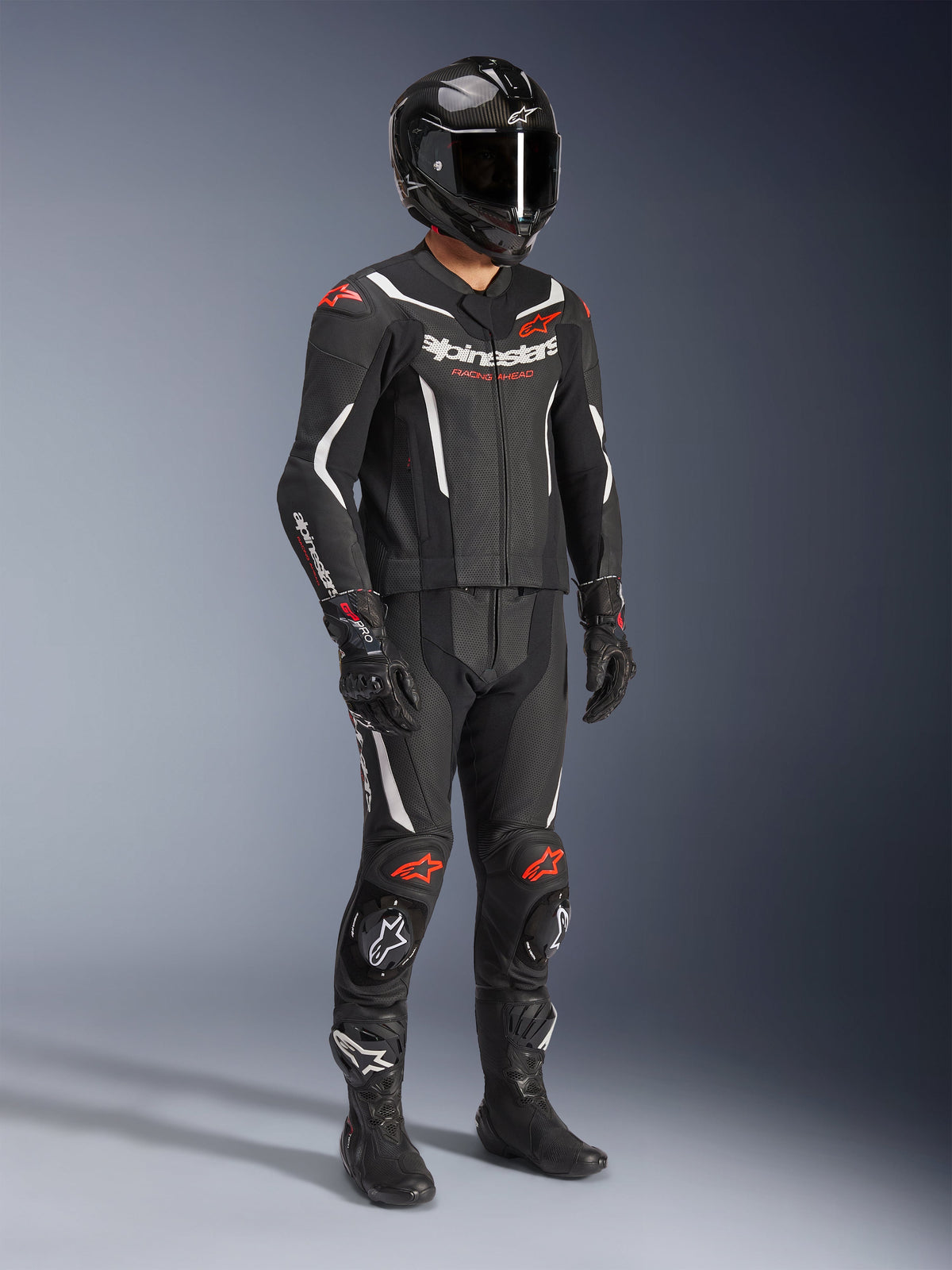 Alpinestars GP Force V2 2-Piece Leather Suit, noir, blanc et rouge fluo, tenue de course de moto complète comprenant un casque en fibre de carbone, des gants de course et des bottes, conception en cuir avec panneaux perforés et bosse aérodynamique.