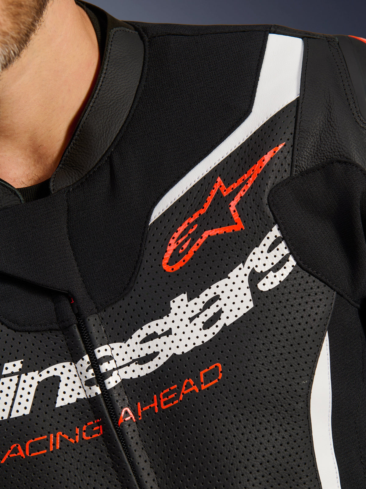 Combinaison en cuir Alpinestars GP Force V2 2 pièces, gros plan sur le torse, cuir perforé noir avec accents blancs et rouges, logo Alpinestars rouge et inscription 'RACING AHEAD', détail d'équipement de course moto haut de gamme