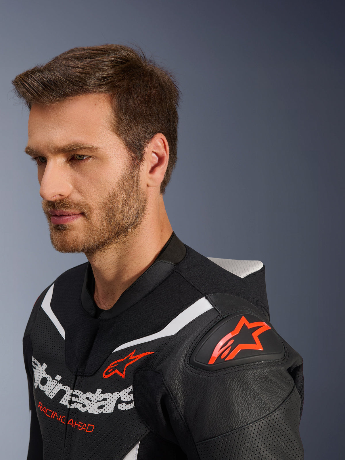 Combinaison en cuir Alpinestars GP Force V2 2 pièces, gros plan de la veste portée par un mannequin homme, noir, blanc et rouge fluo, avec cuir perforé, logo étoile rouge sur l'épaule, bosse aérodynamique et logo Alpinestars sur la poitrine, équipement de course moto professionnel