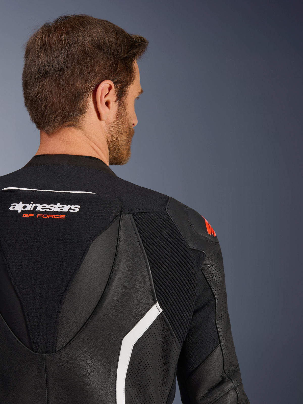 Combinaison en cuir Alpinestars GP Force V2 2 pièces, gros plan du haut du dos et de l'épaule sur un mannequin homme, cuir noir avec accents blancs et rouges, logo Alpinestars GP Force, panneaux perforés et zones extensibles en accordéon pour la course moto