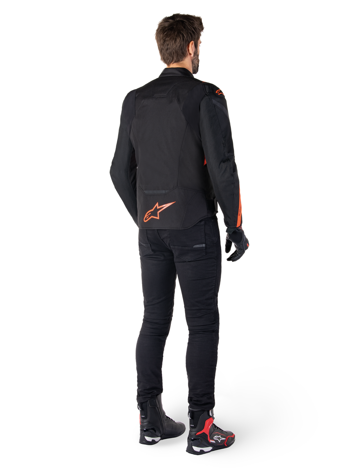 Alpinestars T-Jaws V4 Waterproof Jacket, Black and Red Fluo, rear view worn by a male rider, featuring a vibrant red fluo logo on the back, styled with black riding pants and technical boots, sport motorcycle apparel.