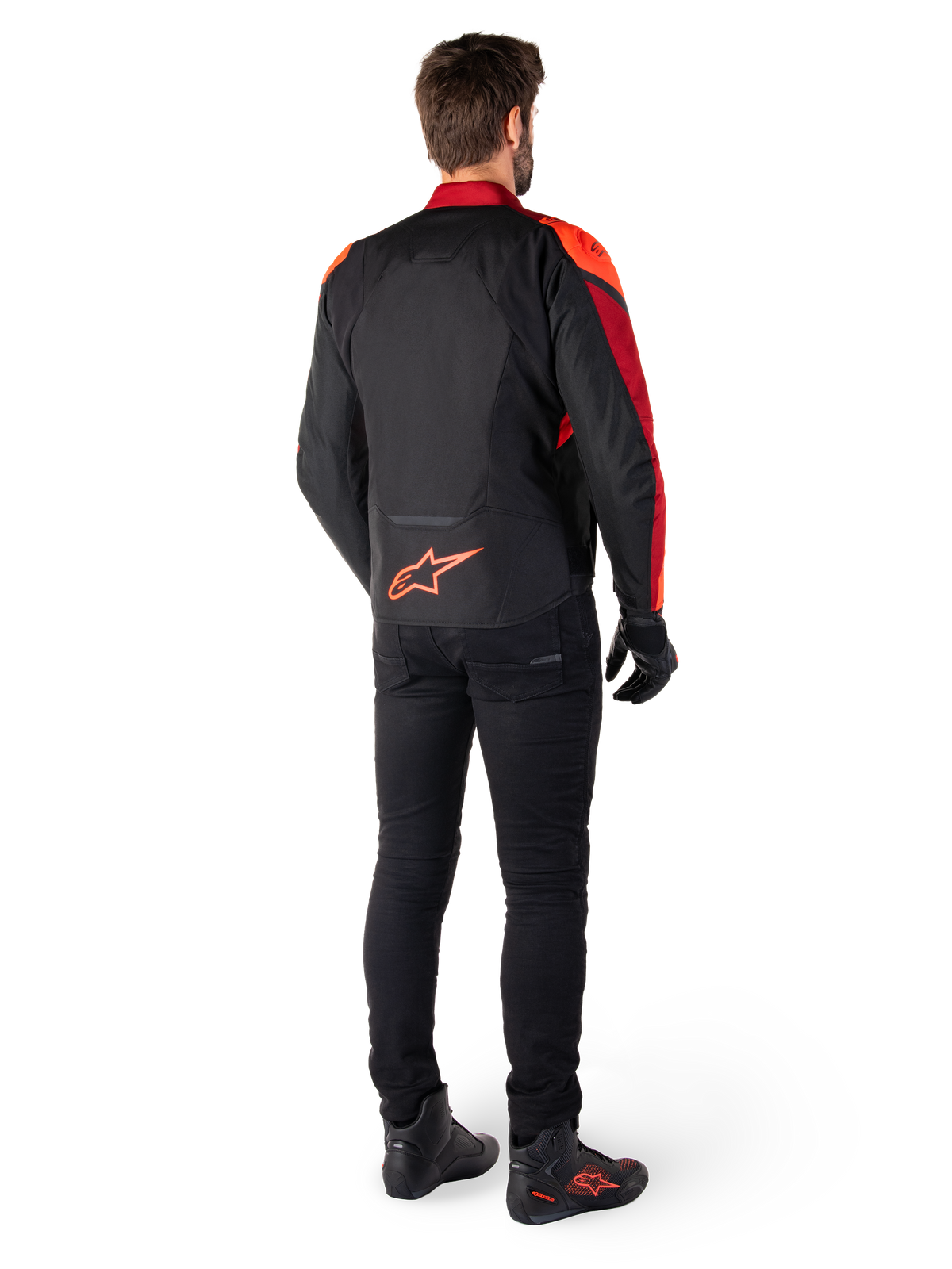 Veste imperméable Alpinestars T-Jaws V4 en Noir Rouge Fluo Rouge Foncé, vue arrière d'un motard portant la veste textile avec un pantalon noir et des bottes de moto, arborant un logo Alpinestars rouge imposant sur le bas du dos.