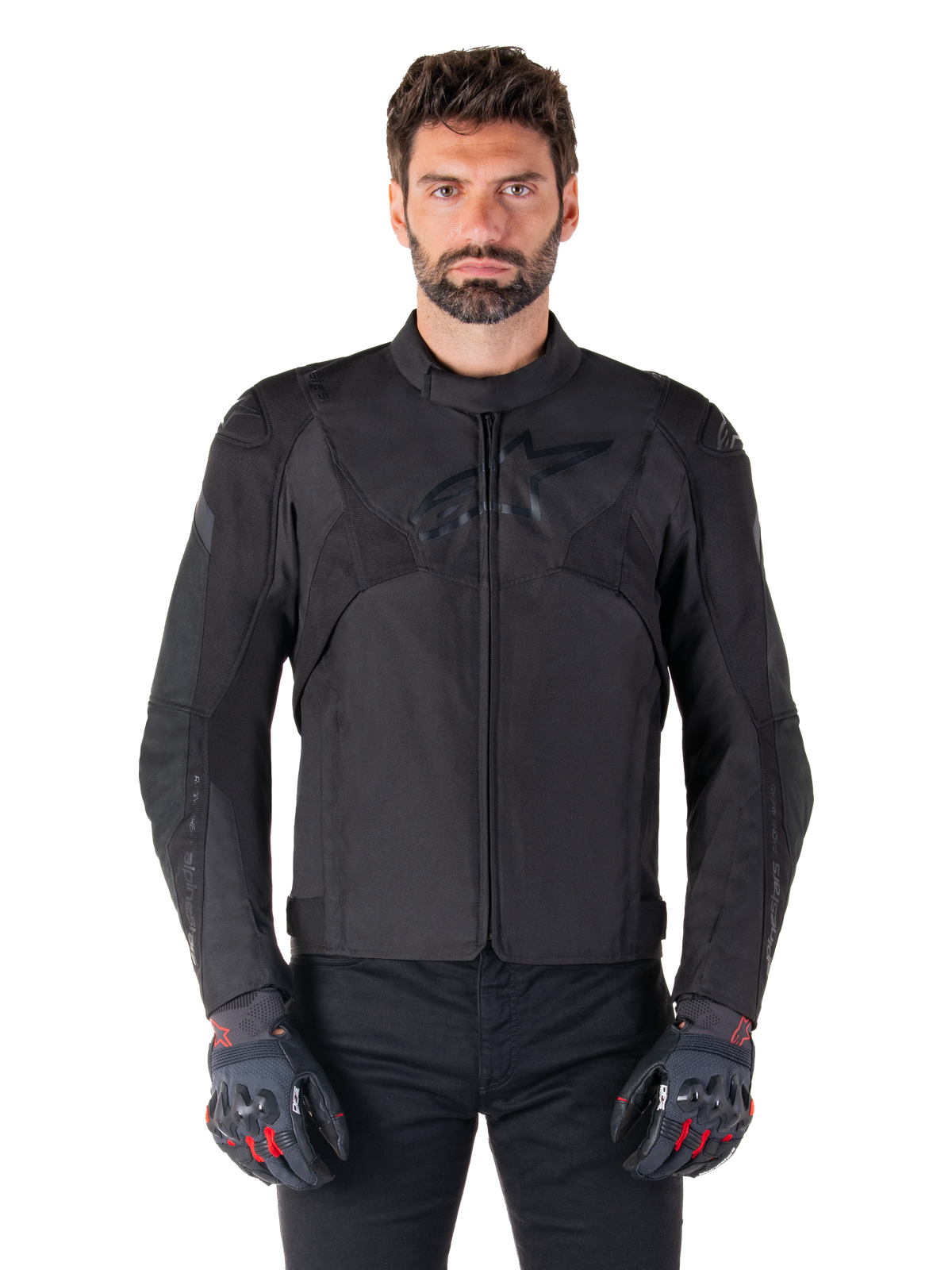 Alpinestars T-Jaws V4 Waterproof Jacket, blouson de moto sport noir, porté par un homme avec des gants noirs aux accents rouges, épaules et bras renforcés, design épuré avec logo discret sur la poitrine, équipement de moto en textile toutes saisons