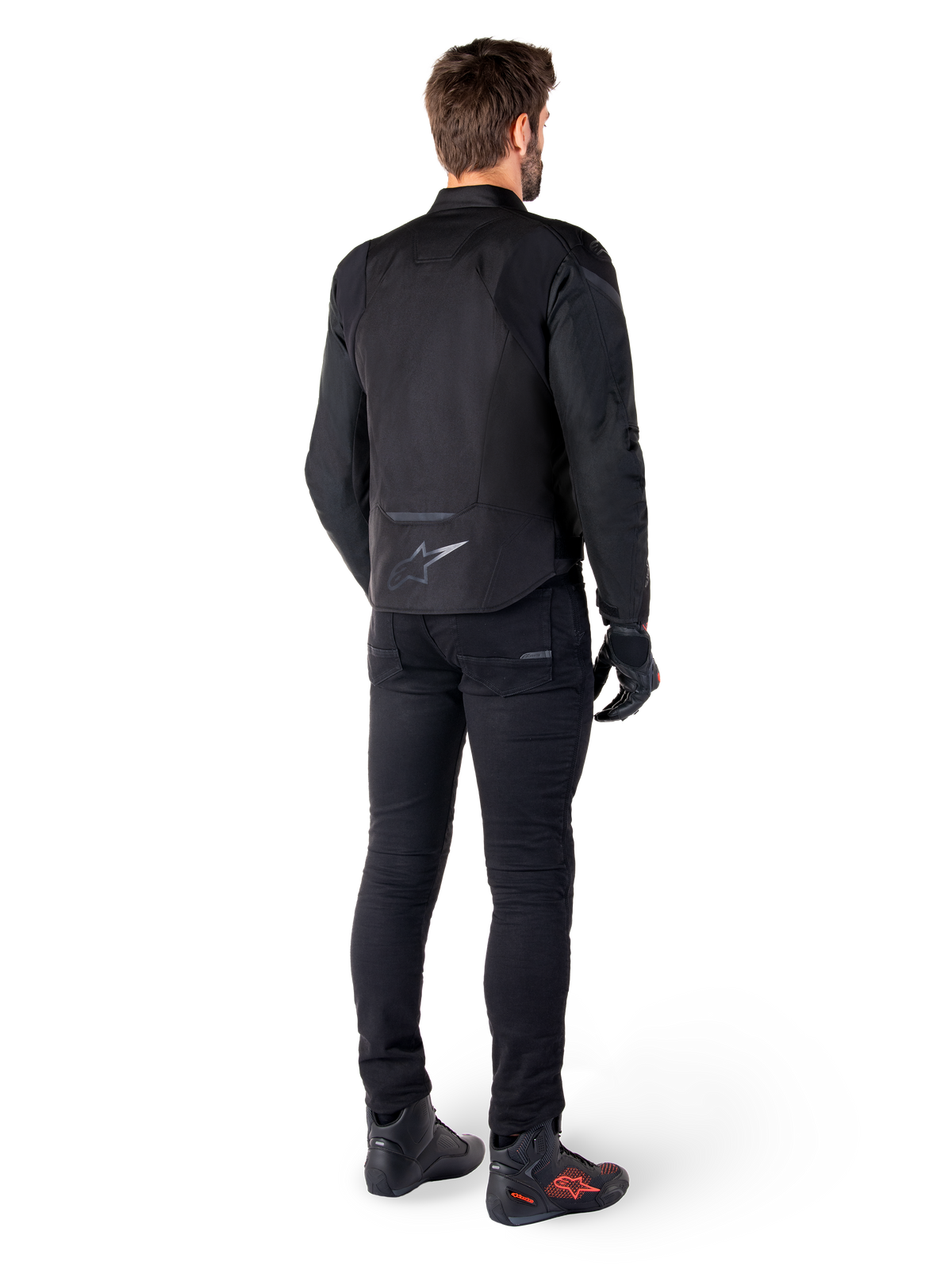 Veste imperméable Alpinestars T-Jaws V4, noire, vue arrière sur un mannequin portant un pantalon et des bottes de moto noirs, mettant en valeur la construction textile sport et le logo Alpinestars sur le bas du dos.
