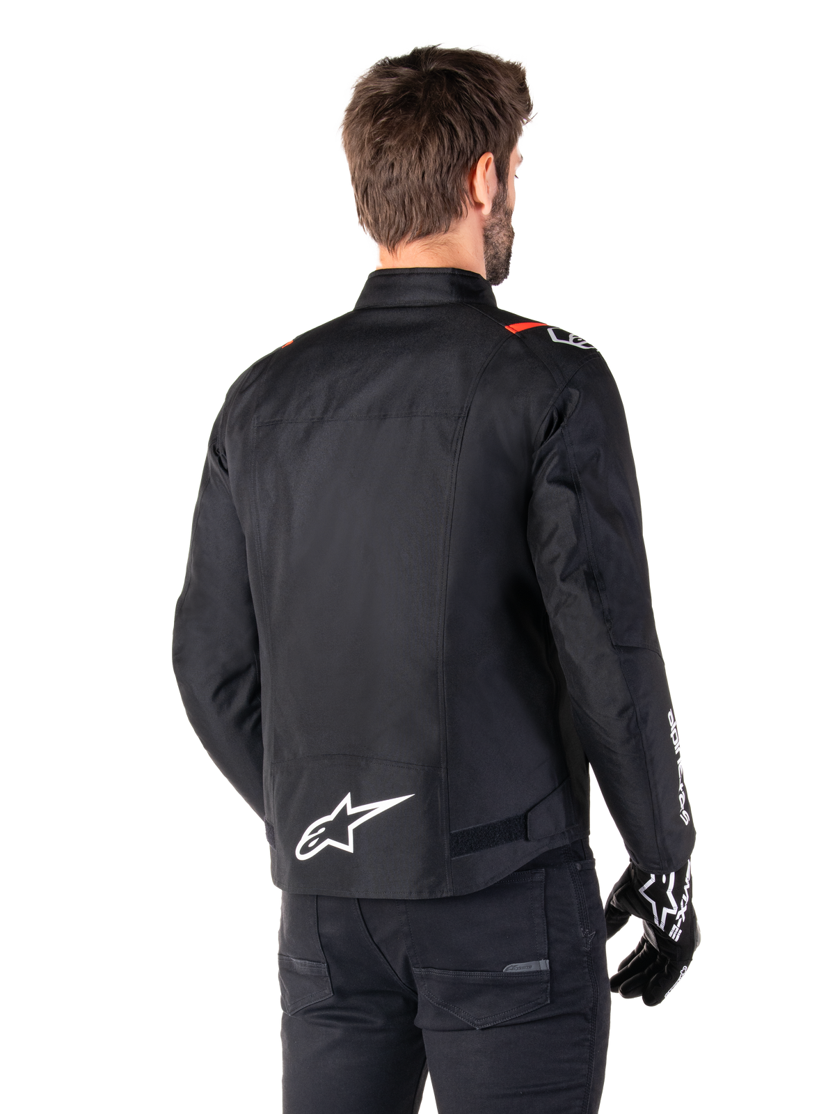 Veste imperméable Alpinestars T-SPS V2, Noir Blanc Rouge Fluo, vue arrière, avec logo Alpinestars blanc en bas du dos et accents rouges sur les épaules, portée avec des gants et un pantalon de moto noirs, veste de moto en textile de style sport.