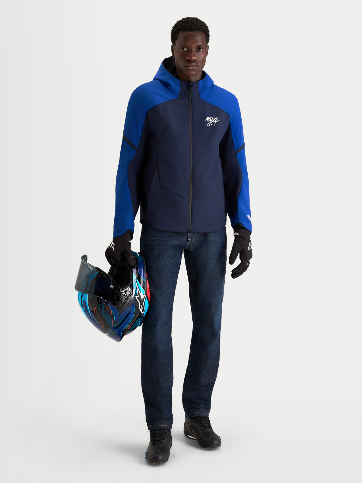 Alpinestars Aeroshell Wp Veste, veste de moto softshell imperméable pour homme bleu marine et bleu vif avec capuche, portée par un modèle tenant un casque assorti