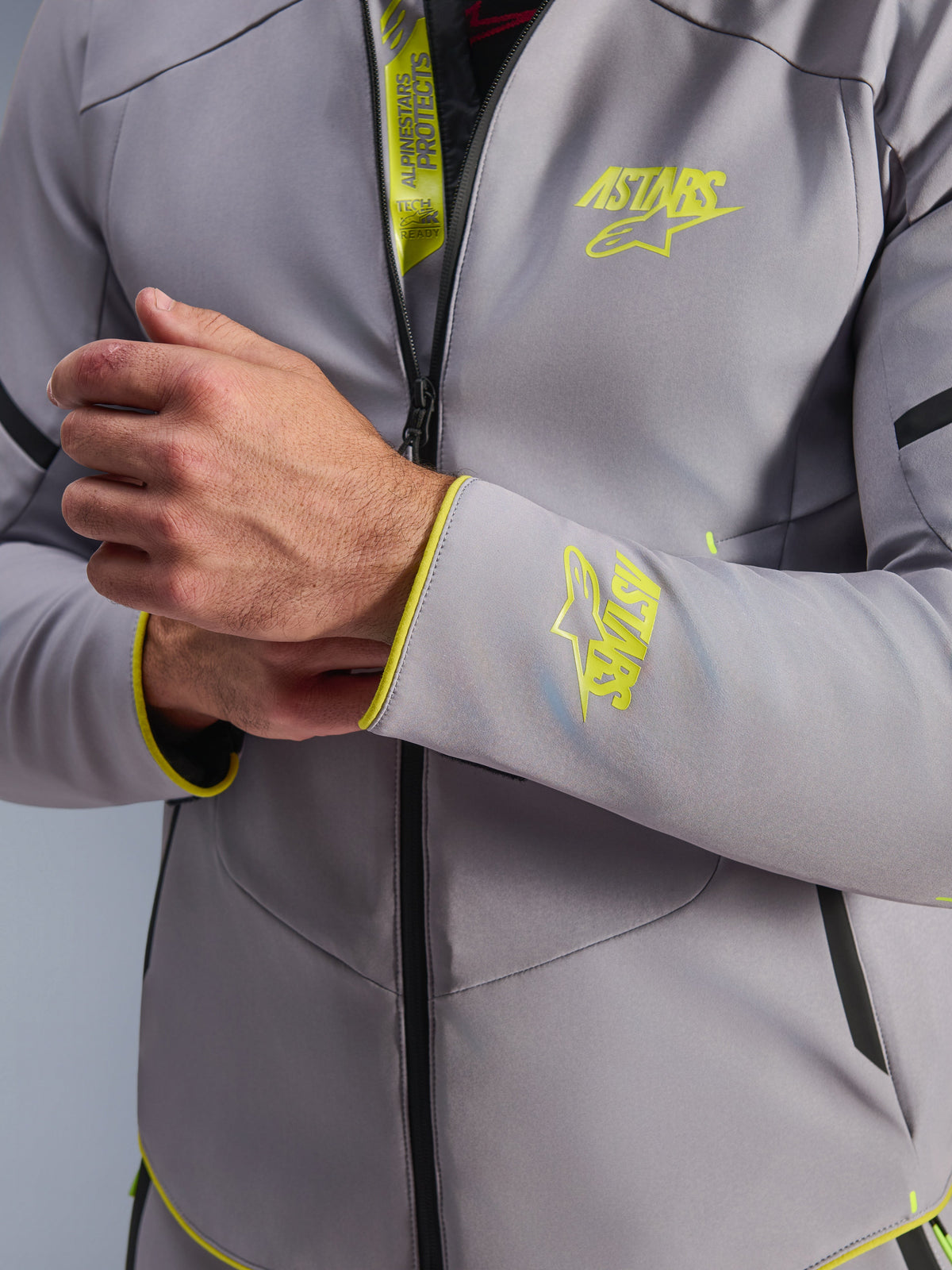 Veste imperméable Alpinestars Aeroshell, gris moyen avec accents jaune fluo, gros plan sur la poitrine et le poignet montrant les logos Astars jaune fluo, détail du rabat interne avec marquage Tech-Air Ready, veste de moto softshell sportive moderne