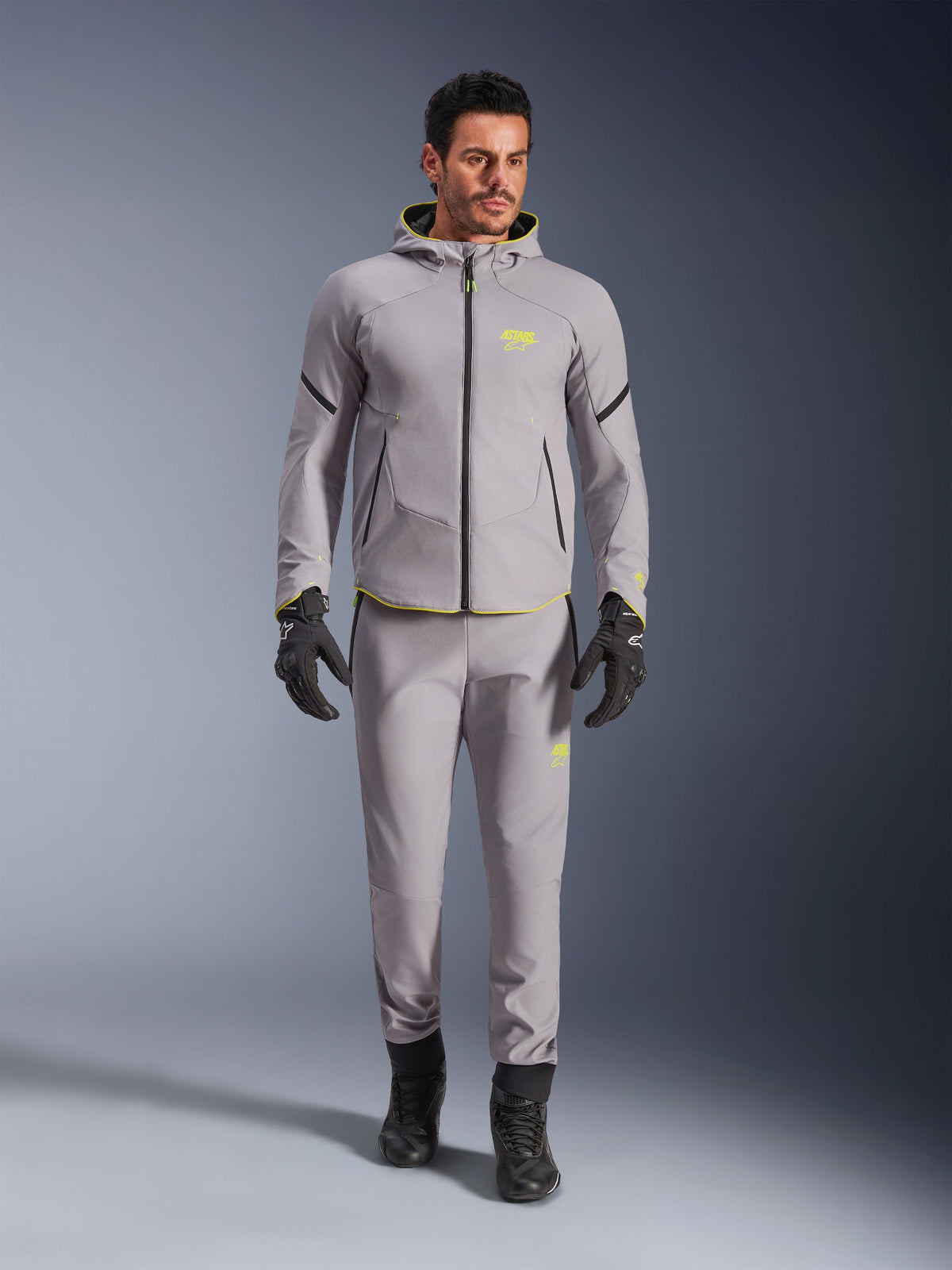 Veste imperméable Alpinestars Aeroshell, Mid Gray Yellow Fluo, portée avec un pantalon gris assorti, des gants et des bottes noirs, dotée d'un design moderne de sweat à capuche d'inspiration sportive avec des touches jaune vif et une coupe athlétique.