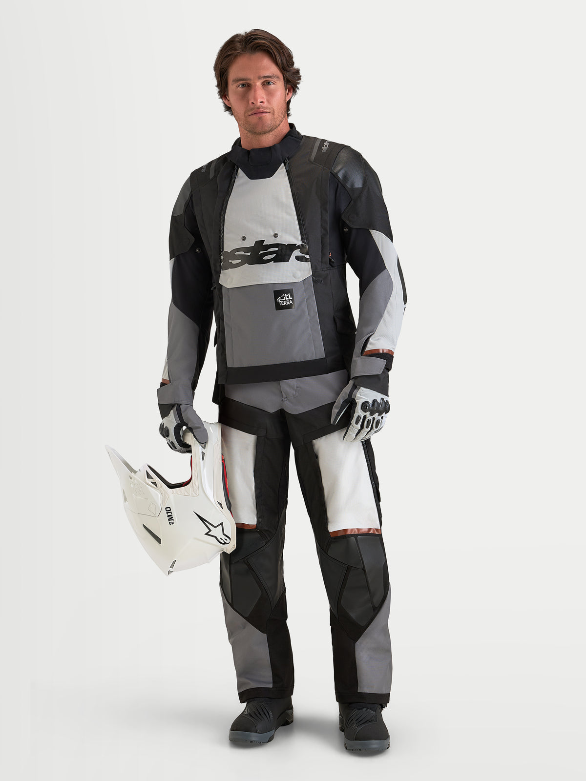 Alpinestars Harok V2 Drystar veste de moto adventure pour homme, gris foncé, gris glacier et noir, construction textile imperméable, portée par un modèle masculin tenant un casque blanc