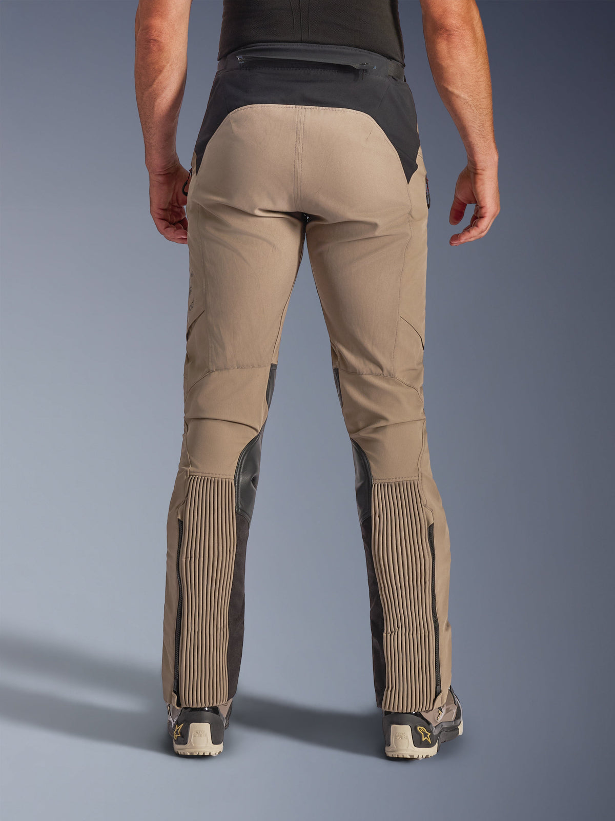 Pantalon Alpinestars AMT-8 Stretch Drystar® XF, Walnut Black, vue arrière sur modèle, châssis en textile extensible beige avec empiècement noir à la taille et panneaux aux mollets, doté de larges sections en accordéon extensible sur le bas des jambes, ouvertures de jambes zippées et coupe adventure-touring