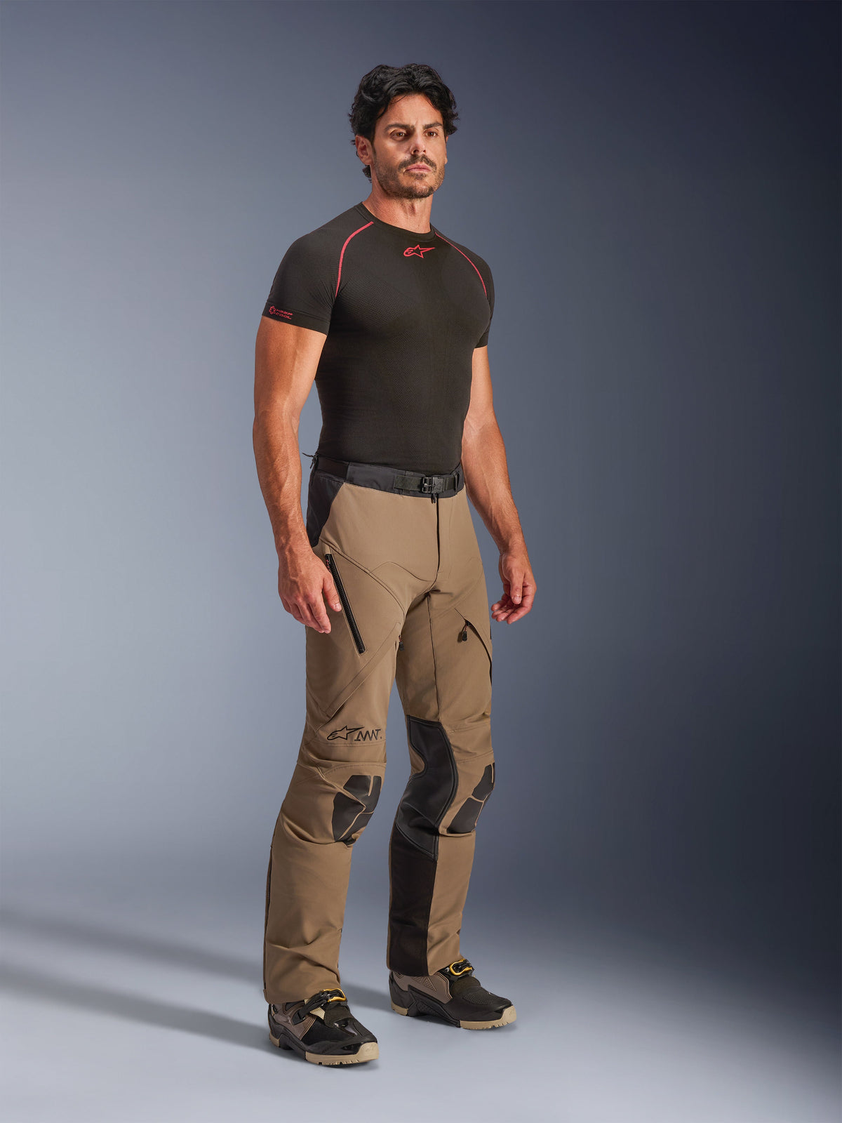 Pantalon Alpinestars AMT-8 Stretch Drystar® XF en Walnut Black, pantalon de moto adventure touring porté par un mannequin avec un t-shirt technique noir, doté d'un tissu extensible, d'ouvertures de ventilation zippées aux cuisses et de panneaux de protection aux genoux.