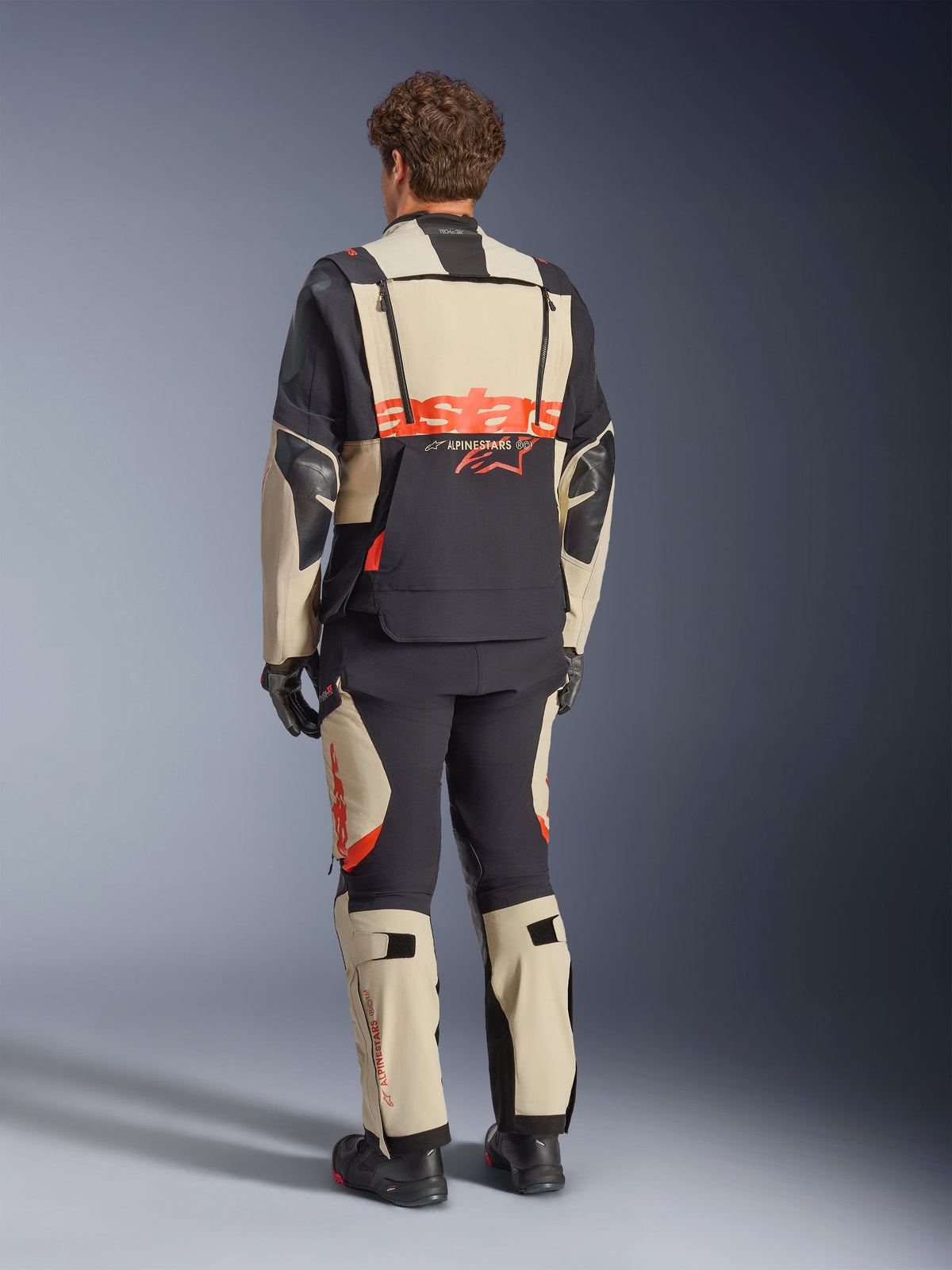 Veste laminée Alpinestars Halo Pro Drystar® XF, Mastic Black, vue de dos, veste de moto d'aventure avec un grand logo 'astars' orange à l'arrière, portée avec un pantalon technique et des bottes assortis, design modulaire pour terrains variés