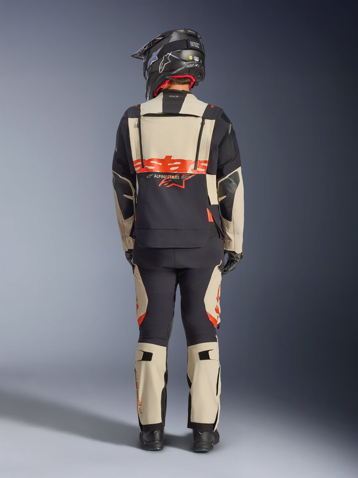 Veste laminée Alpinestars Halo Pro Drystar® XF, veste de moto d'aventure, noir mastic, vue arrière d'un motard portant un pantalon assorti et un casque noir, avec marquage Alpinestars orange vif et panneaux de ventilation modulaires pour une conduite d'aventure polyvalente.