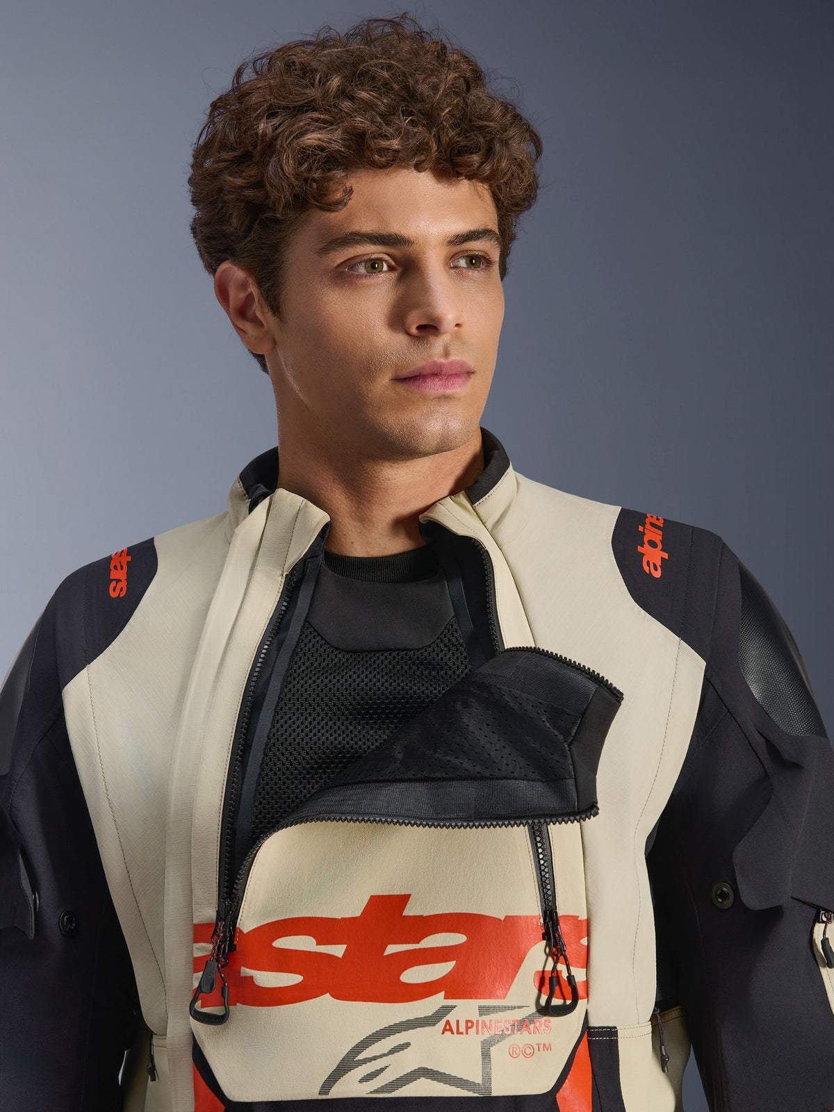Veste laminée Alpinestars Halo Pro Drystar® XF en Mastic Black, modèle masculin portant la veste avec le panneau de ventilation de la poitrine ouvert révélant la sous-couche en maille, marquage rouge et empiècements noirs aux épaules, équipement technique de moto d'aventure