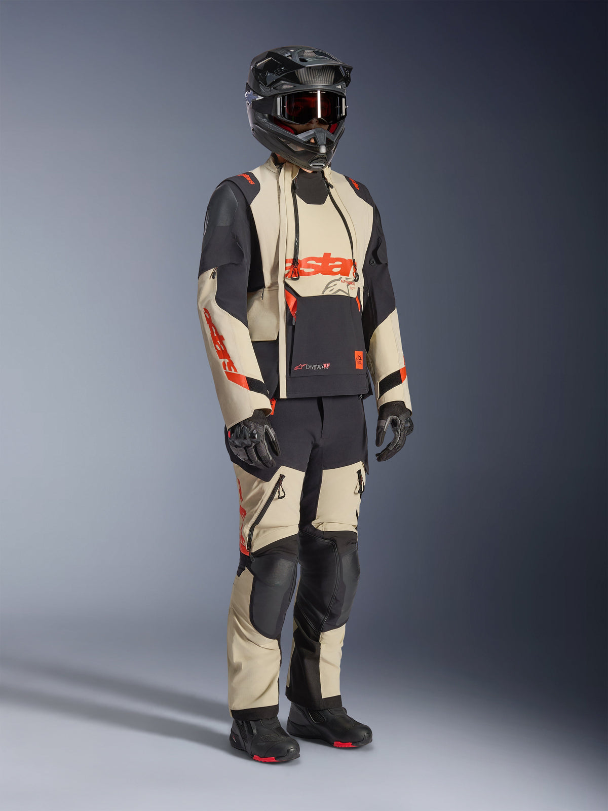 Veste laminée Alpinestars Halo Pro Drystar® XF en Mastic Black, veste de moto d'aventure portée avec un pantalon assorti, un casque intégral, des gants et des bottes, présentant des panneaux beige et noir avec des logos rouges, conception technique multi-saison.