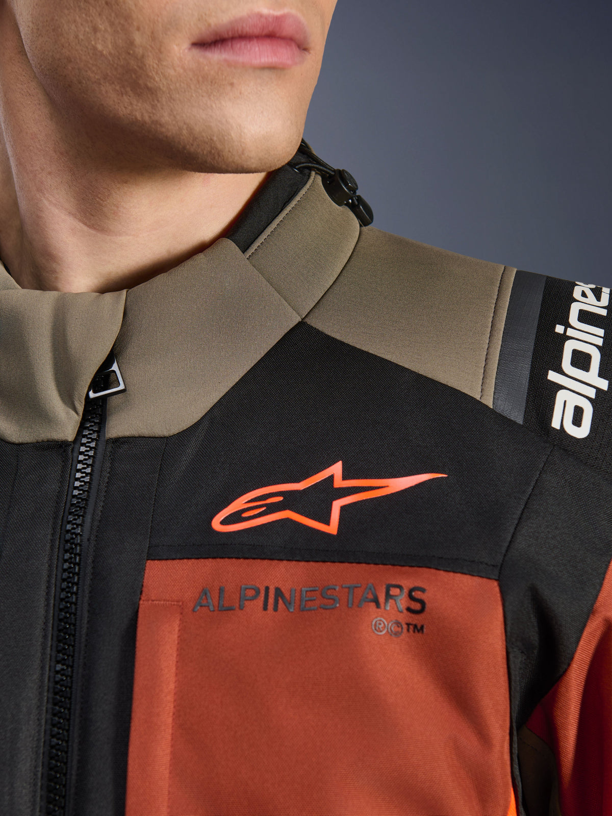 Veste Alpinestars Andes V4 Drystar® en Walnut Rust Black, gros plan sur le haut de la poitrine et l'épaule, avec logo A-star orange sur empiècement noir et marquage Alpinestars sur la section couleur rouille, détail d'équipement de moto d'aventure