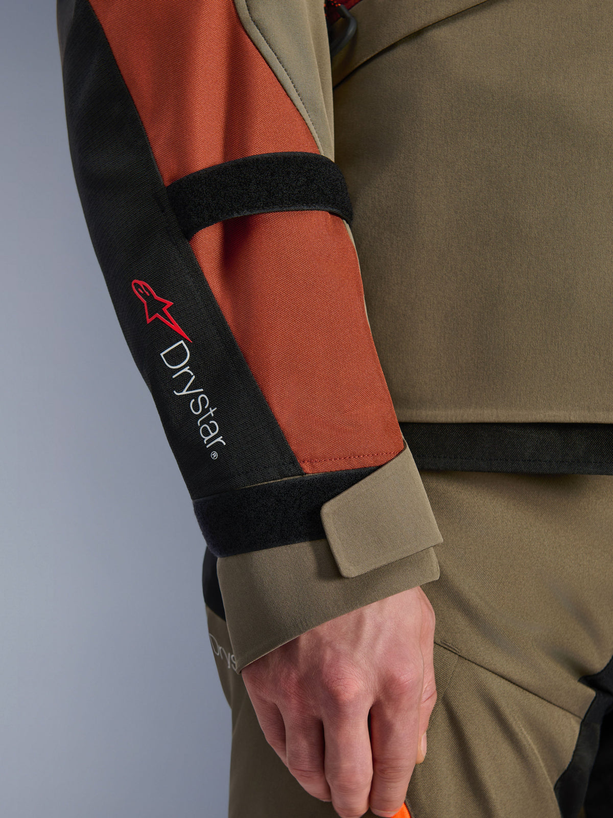 Veste Alpinestars Andes V4 Drystar®, veste de moto, Walnut Rust Black, vue rapprochée de la manche avec marquage Drystar® et logo étoile rouge, sangles velcro réglables à l'avant-bras et au poignet, conception textile durable pour le touring d'aventure