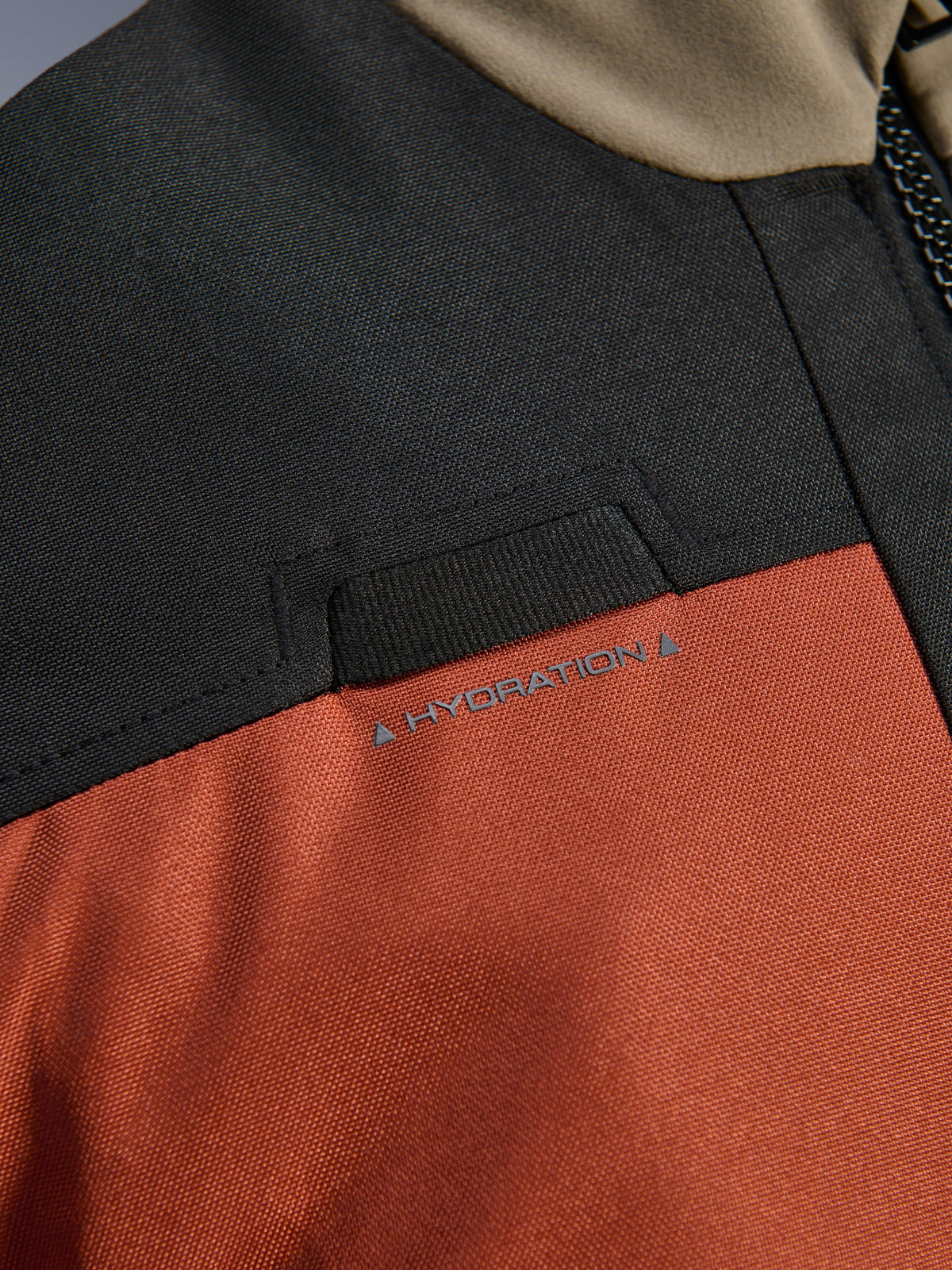 Détail en gros-plan de la veste Alpinestars Andes V4 Drystar® Walnut Rust Black, mettant en avant la boucle pour tuyau d'hydratation intégrée sur la poitrine et la construction en textile ripstop durable.