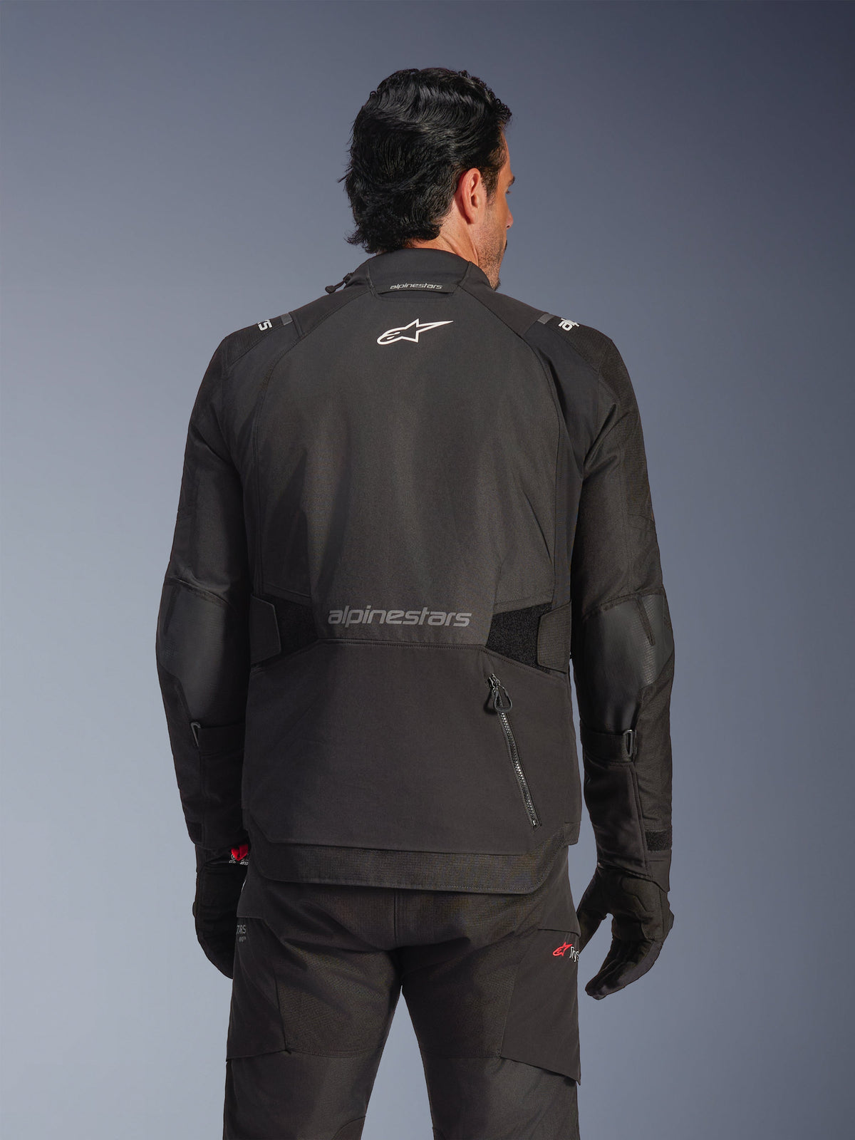 Veste Alpinestars Andes V4 Drystar®, noire, vue arrière sur un mannequin, veste d'aventure en textile avec logos réfléchissants et une poche arrière zippée, portée avec un pantalon et des gants noirs assortis
