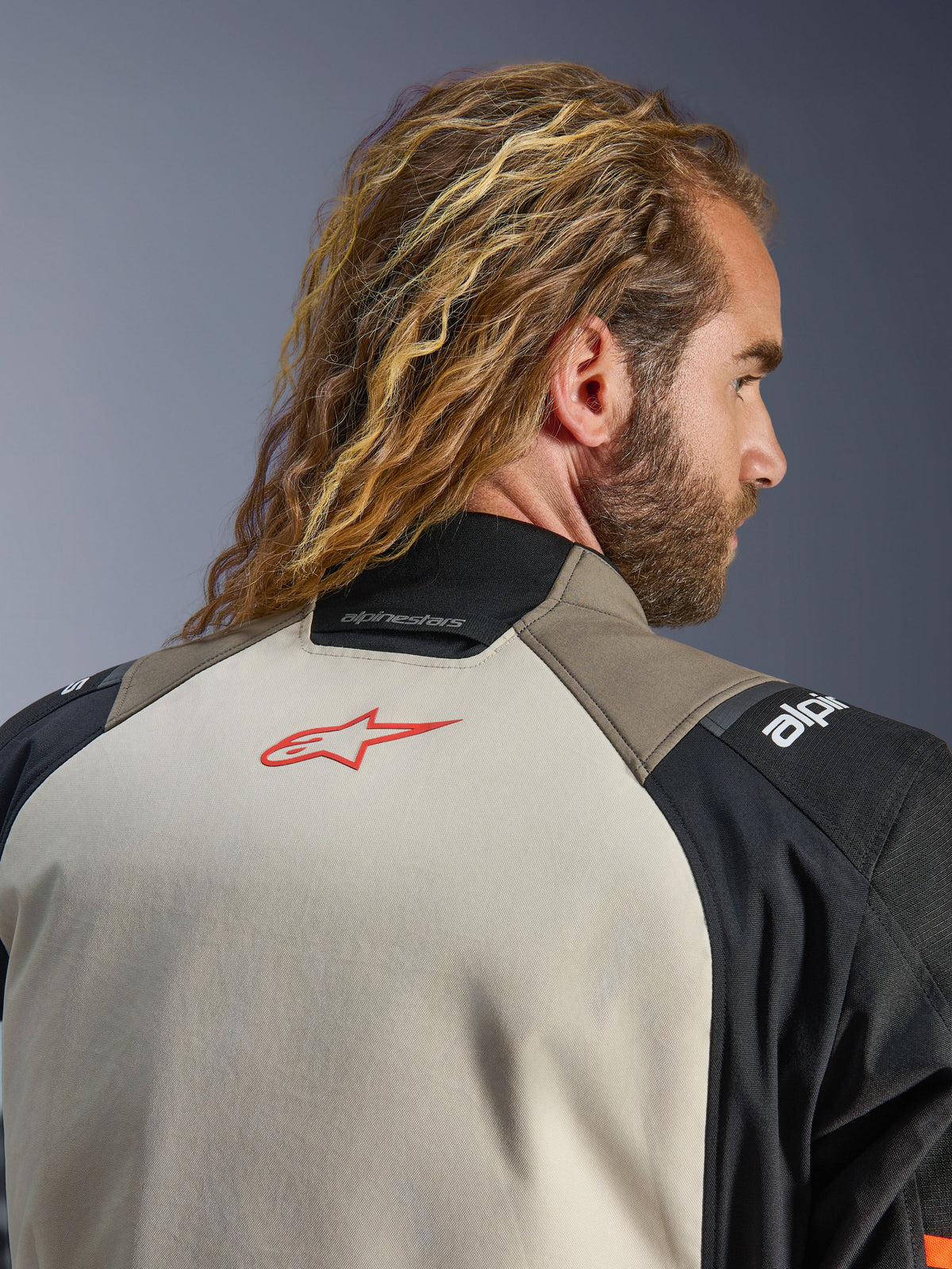 Veste Alpinestars Andes V4 Drystar®, coloris Walnut Mastic Black, vue rapprochée du haut du dos et du col, avec un logo étoile rouge sur l'empiècement mastic, construction textile walnut et noir, équipement de moto touring aventure