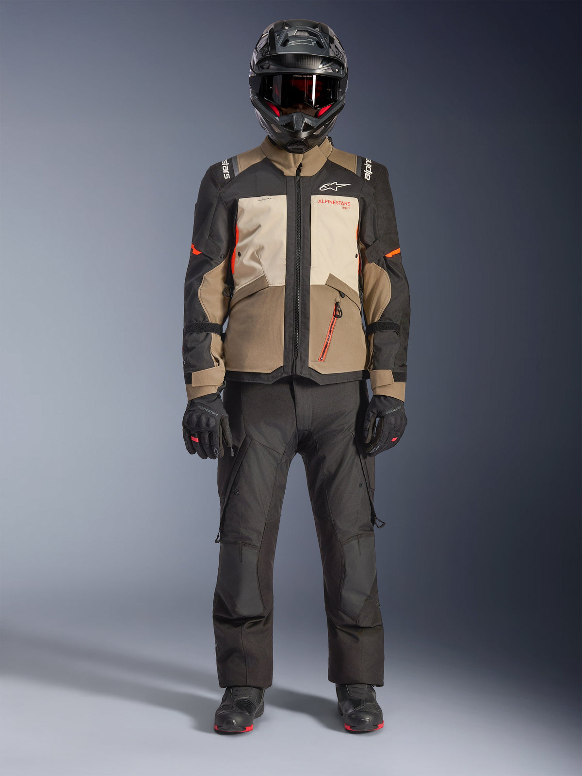 Veste Alpinestars Andes V4 Drystar®, Walnut Mastic Black, veste de moto adventure touring avec panneaux beige et crème et accents orange, portée par un pilote avec un casque d'aventure noir, un pantalon de moto noir et des bottes noires, vue studio en pied