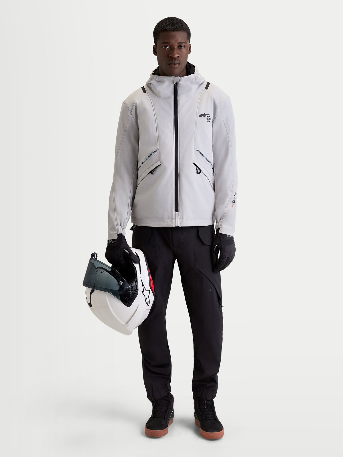 Alpinestars C 5 Drystar Veste, veste de moto urbaine contemporaine pour homme en gris clair et noir, vue de face d'un modèle portant la veste imperméable avec capuche intégrée et tenant un casque