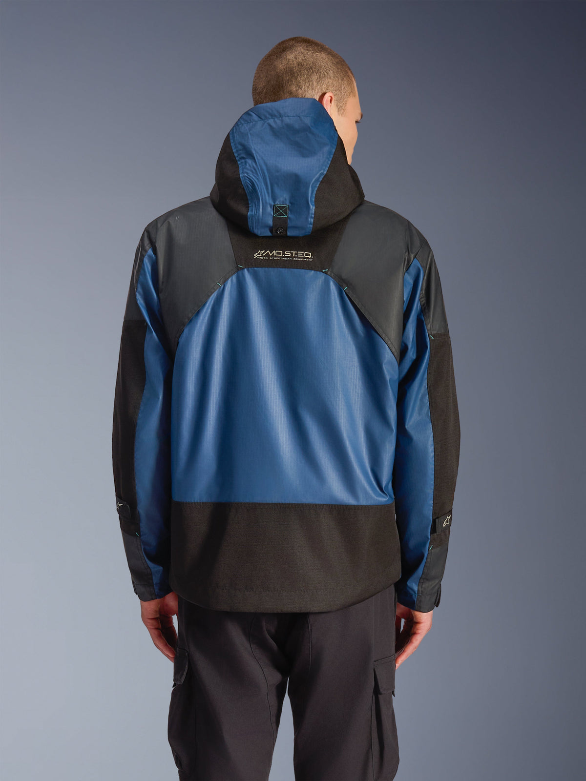 Veste imperméable Alpinestars Mospher en Noir Dark Petrol, vue arrière d'une parka de moto avec panneaux en ripstop bleu et sections renforcées noires, marquage MO.ST.EQ. sur le haut du dos, design tactique urbain moderne