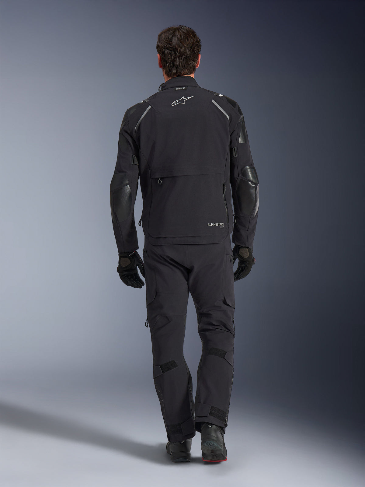 Alpinestars Andes Pro Drystar® XF Jacket, adventure touring jacket, Black and Dark Gray, rear view showing large cargo pocket and reinforced elbow panels, worn with matching black pants and gloves, sleek functional design for all-weather riding