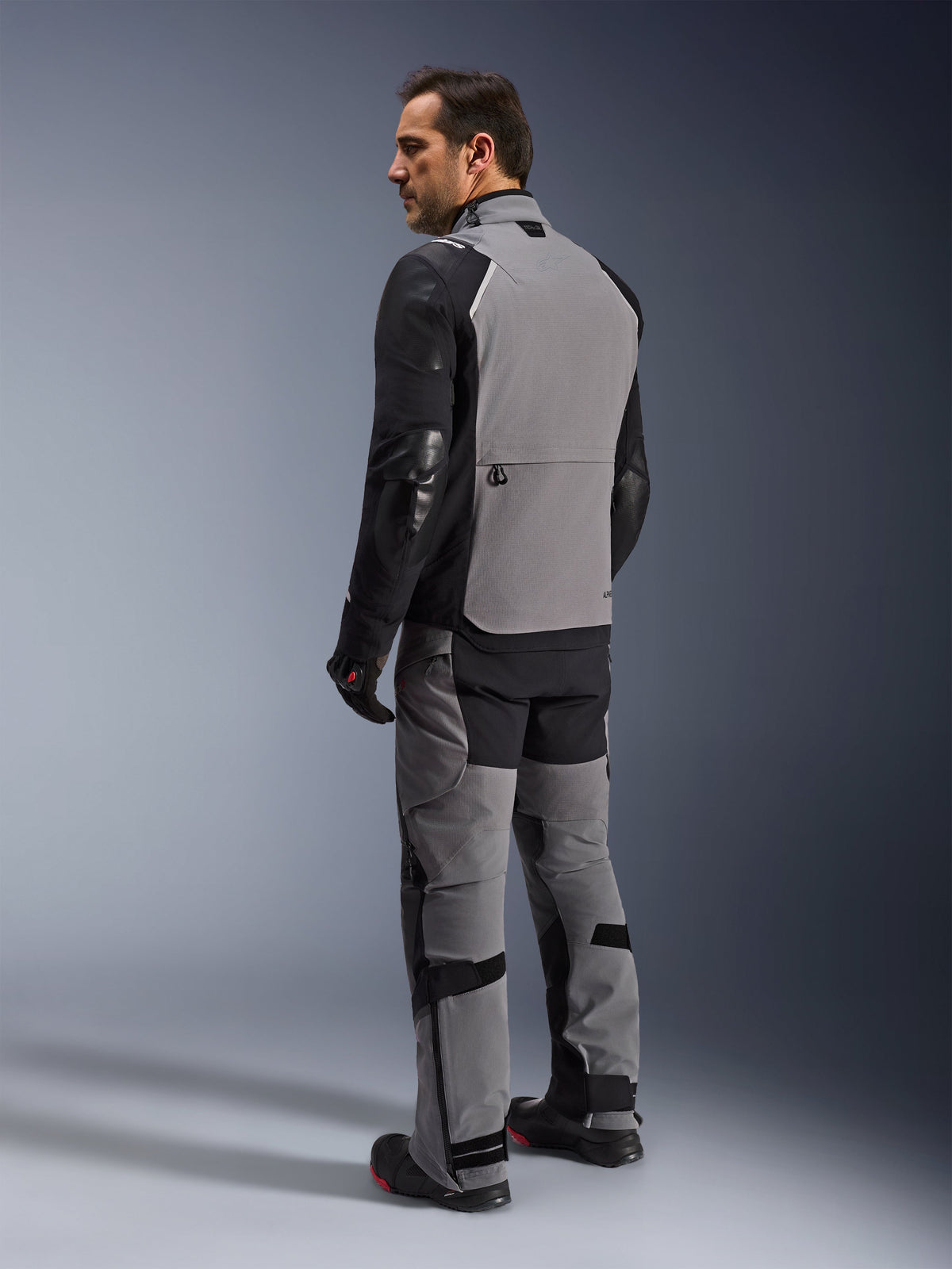 Veste Alpinestars Andes Pro Drystar® XF, veste de moto adventure-touring en gris foncé et noir, vue de dos sur un mannequin montrant le grand panneau arrière et les manches renforcées, accompagnée du pantalon d'aventure, des gants et des bottes assortis