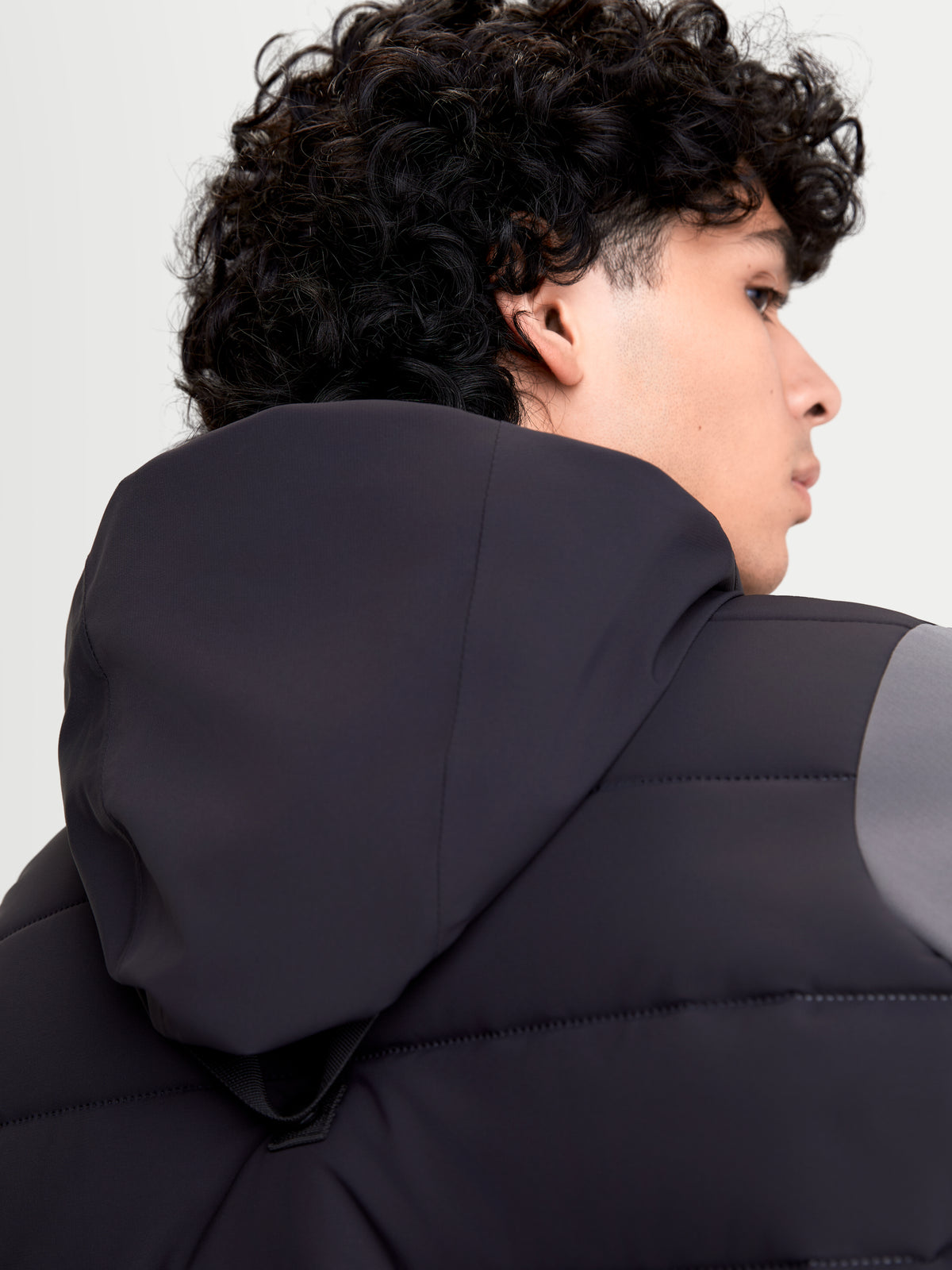 Alpinestars Therma-Tech Waterproof Jacket, men's urban motorcycle jacket in black and dark gray, close-up back view showing the integrated hood system and sonic-welded down construction worn by a model.