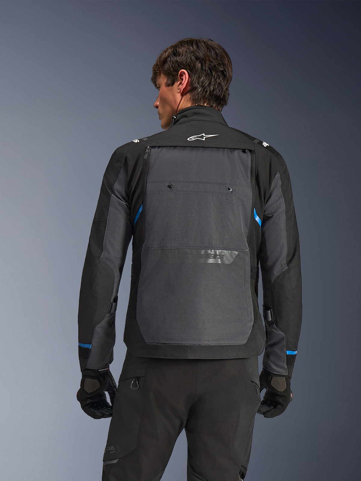 Veste Alpinestars Cusco Drystar®, veste de moto, noir et gris foncé, vue de dos sur un modèle montrant un large panneau arrière gris, logo Alpinestars blanc et accents bleus sur les manches.