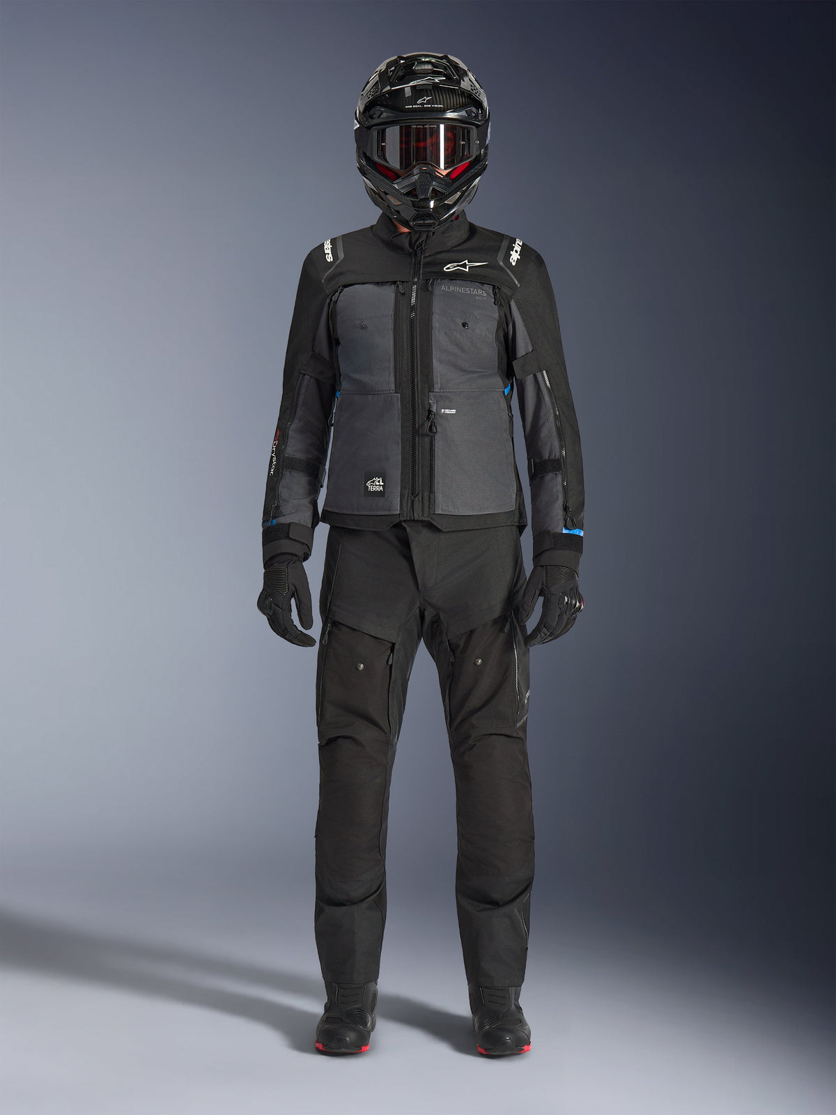 Veste Alpinestars Cusco Drystar®, veste d'aventure touring noir et gris foncé, portée avec un pantalon noir, des gants et un casque intégral assortis, vue de face en pied, vêtement de protection pour moto