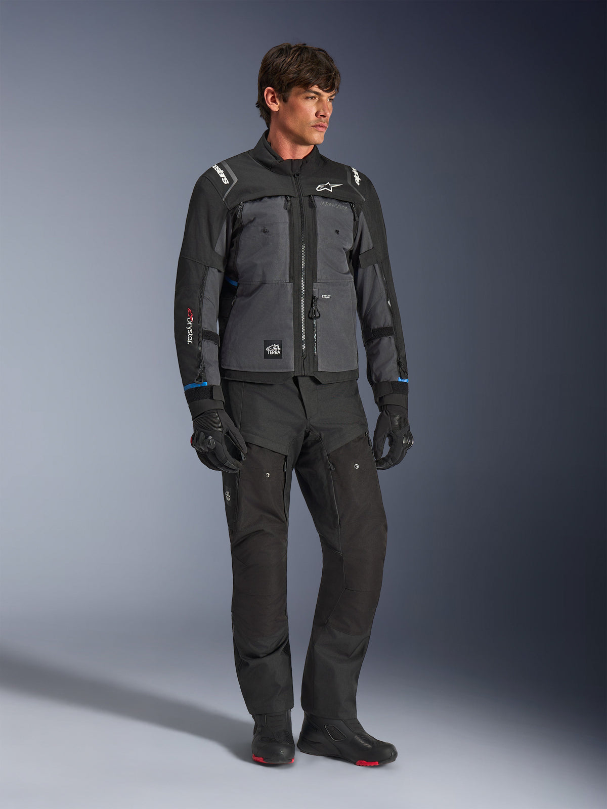Veste Alpinestars Cusco Drystar® en noir et gris foncé, veste technique de touring moto avec empiècements multi-tons, portée avec un pantalon et des gants de moto noirs assortis, conçue pour la route et l'adventure touring.