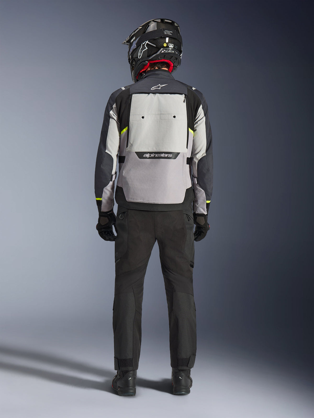 Motard vu de dos portant la veste Alpinestars Cusco Drystar® en Ice Gray, Mid Gray et Deep Gray, dotée d'un large panneau de ventilation dorsal et du logo Alpinestars, avec un pantalon de moto noir et un casque noir, équipement de moto adventure touring