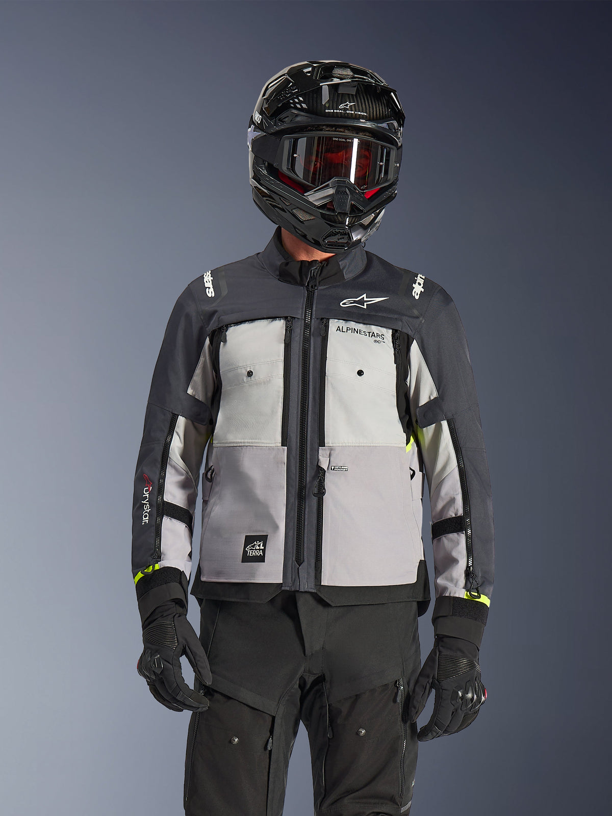 Veste Alpinestars Cusco Drystar®, veste d'aventure touring, coloris Ice Gray Mid Gray et Deep Gray, dotée de panneaux gris multi-tons, de ventilations zippées sur la poitrine et du marquage Alpinestars, portée par un pilote avec un casque et un masque noirs.