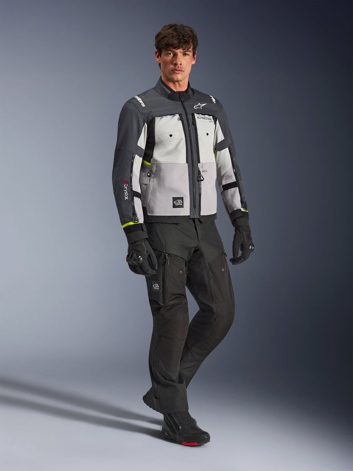 Veste Alpinestars Cusco Drystar®, veste de moto aventure, Ice Gray, Mid Gray et Deep Gray, portée par un mannequin avec pantalon et gants noirs, panneaux gris multi-tons avec construction textile durable, dotée d'aérations zippées et du marquage Alpinestars, photographie professionnelle en studio pour équipement de route et d'aventure