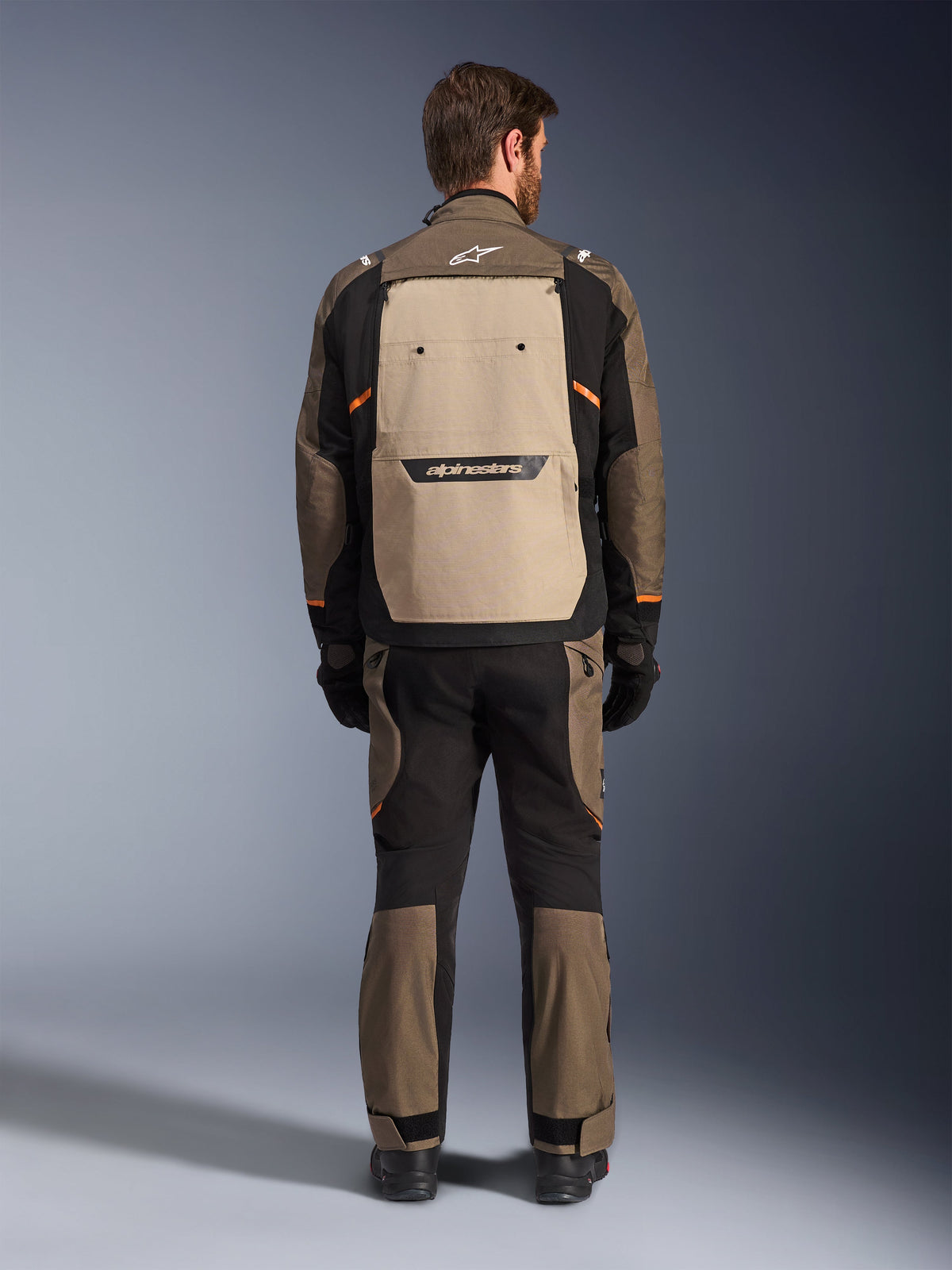 Veste Alpinestars Cusco Drystar®, vue arrière, Walnut Aluminum Black, équipement de touring aventure en textile, large panneau de ventilation arrière beige avec logo noir, accents orange, portée avec pantalon et gants assortis