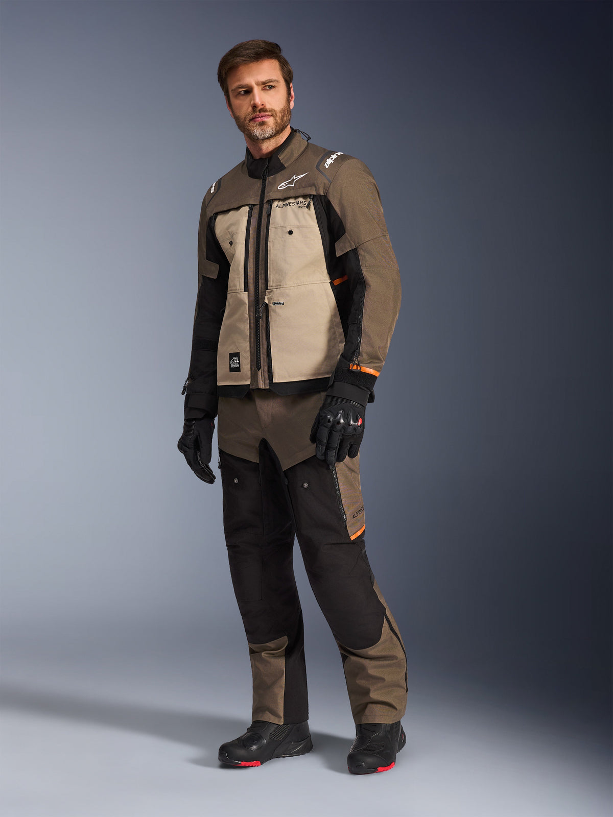 Veste Alpinestars Cusco Drystar® en Walnut Aluminum Black, portée par un mannequin homme avec un pantalon et des gants de moto assortis, design adventure-touring avec empiècements beiges sur la poitrine et détails noirs.