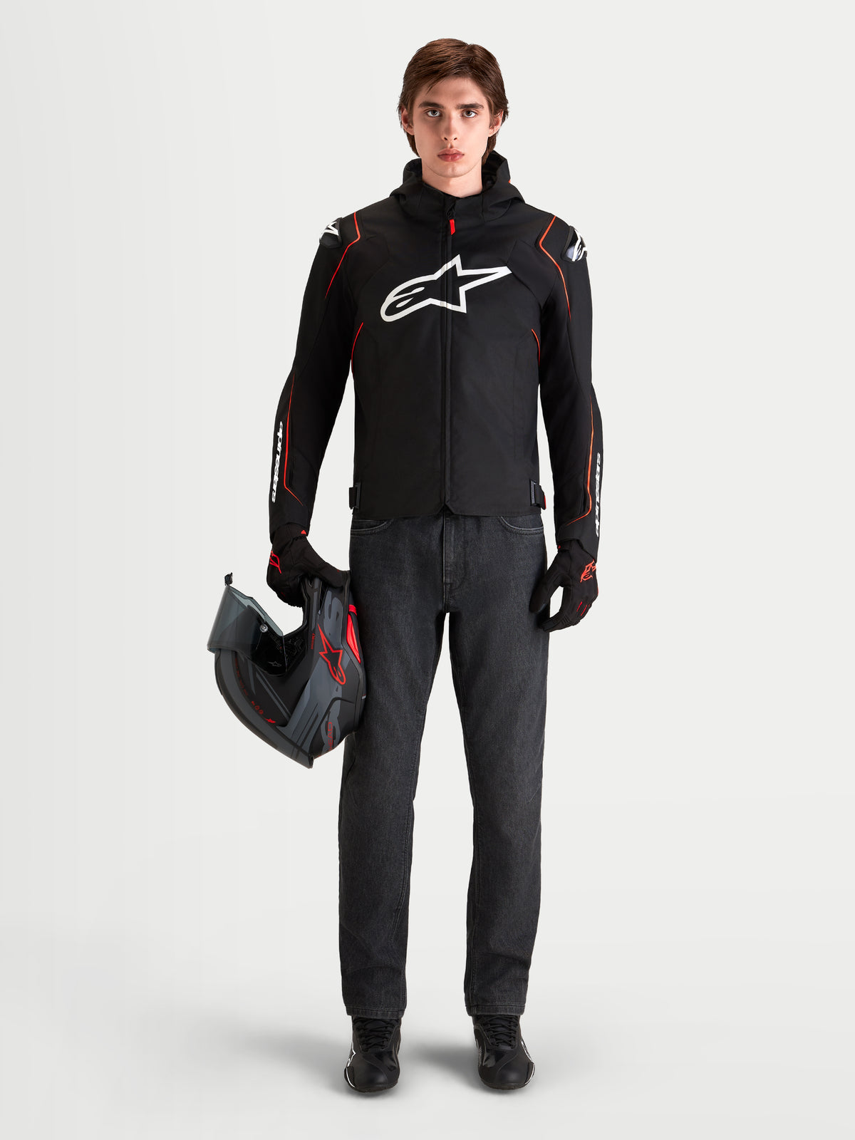 Alpinestars Zaca V 2 Waterproof, veste de moto sport imperméable pour homme, noire et rouge, avec protections d'épaules DFS et capuche intégrée, portée par un modèle tenant un casque