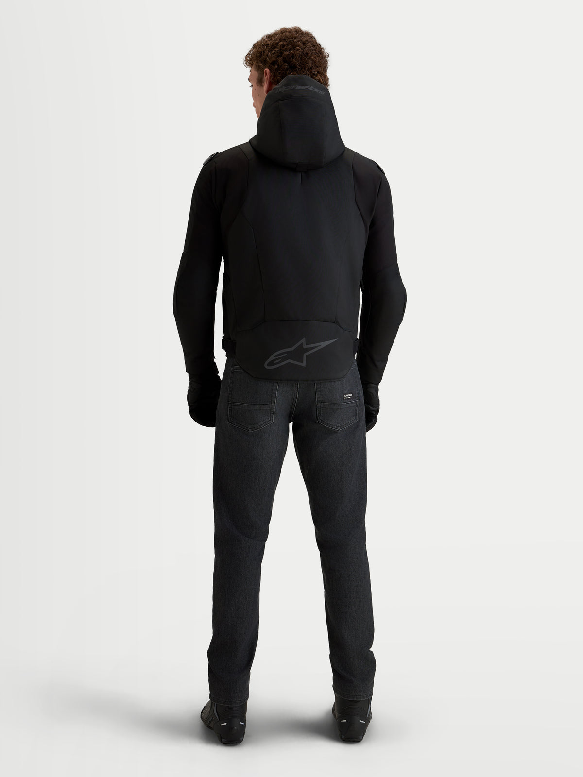 Alpinestars Zaca V2 Waterproof Jacket, Men's Black motorcycle jacket shown from the back, featuring an integrated hood, extended rear hem with tonal Alpinestars logo, and protective riding gear construction