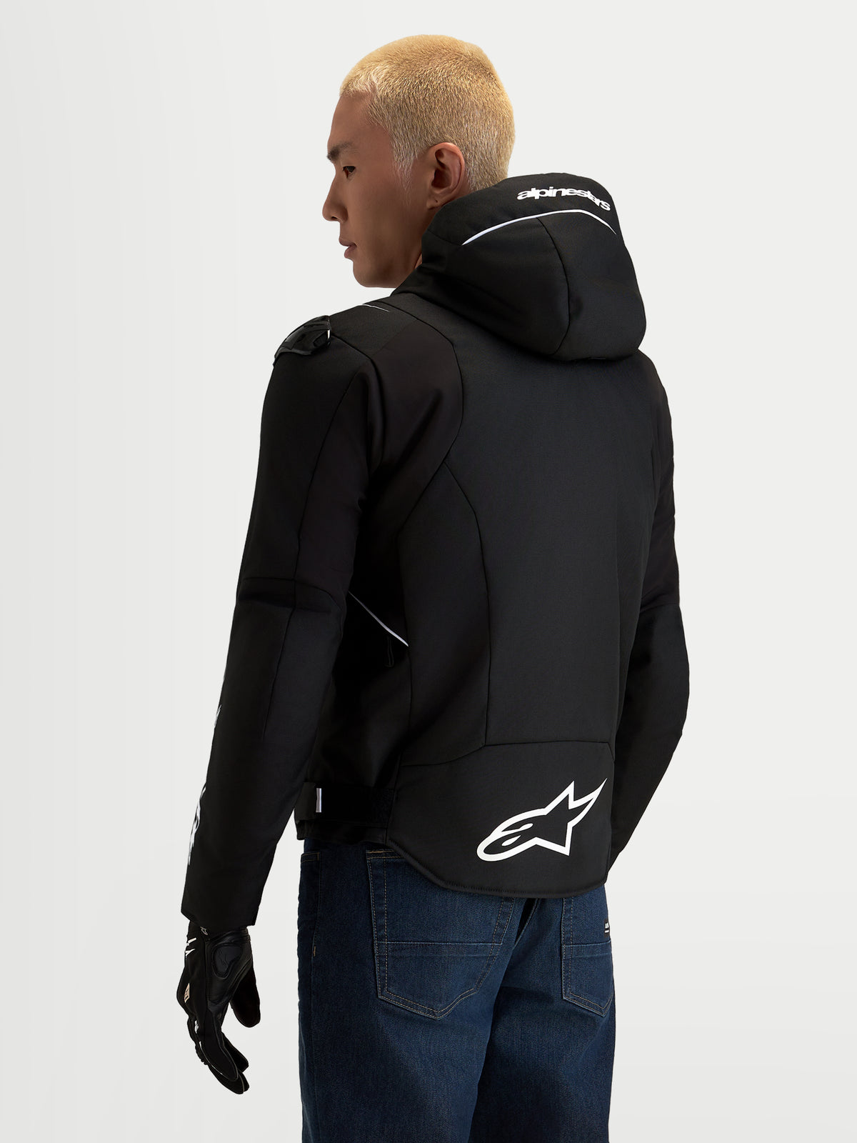 Alpinestars Zaca V2 Waterproof Veste, veste de moto textile pour homme noire et blanche, vue de dos montrant la capuche intégrée avec le marquage Alpinestars blanc, l'ourlet arrière prolongé avec le grand logo A-star et les détails de protection d'épaule