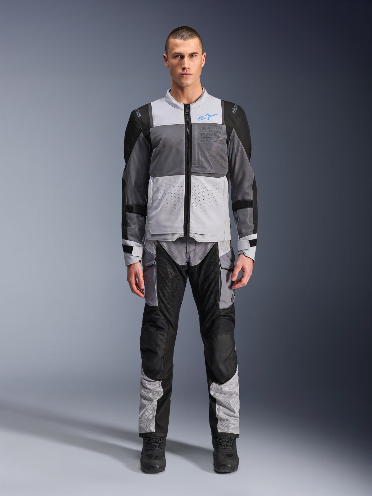 Veste Alpinestars ST-2 Air, veste de touring moto, Gris Glace, Gris Foncé et Noir, portée par un mannequin avec un pantalon d'aventure assorti, avec de larges panneaux en mesh, logo Alpinestars bleu sur la poitrine et marquage Alpinestars Exploration Equipment