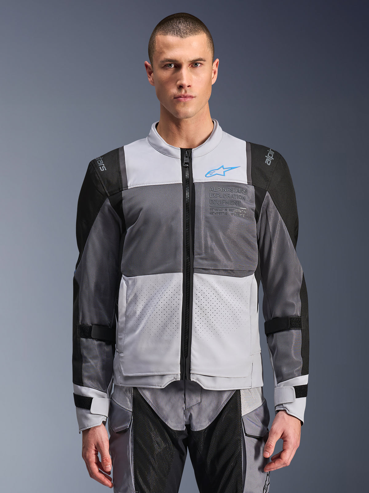 Veste Alpinestars ST-2 Air, veste de moto pour homme, gris glace et gris foncé avec des touches de noir, larges panneaux de ventilation en mesh, avant perforé au laser, logo Alpinestars bleu, fermeture éclair avant, portée par un mannequin avec un pantalon de moto assorti