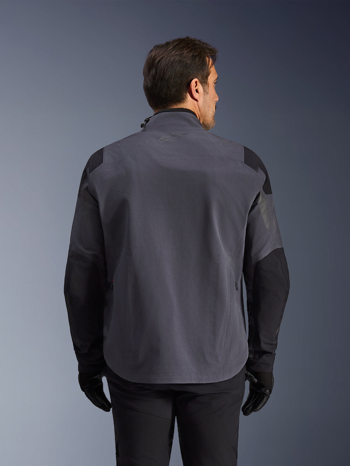 Alpinestars Maxdura Drystar®XF Laminated Armored Shell, technical adventure jacket, Deep Gray and Black, rear view featuring reinforced shoulder and elbow panels, subtle logo on the upper back, worn with black gloves and pants, engineered for all-weather protection