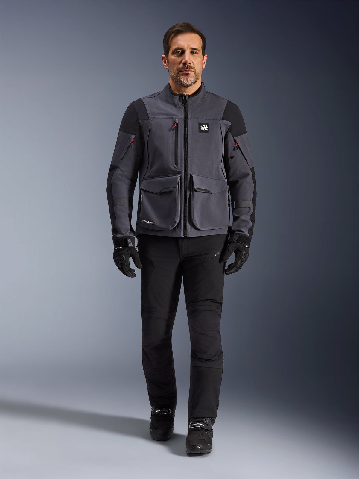 Maxdura Drystar®XF Laminated Armored Shell, Motorcycle Jacket, Deep Gray Black, worn by a model with black pants and gloves, featuring large cargo pockets, red zipper accents, and All Terra branding, technical adventure riding gear