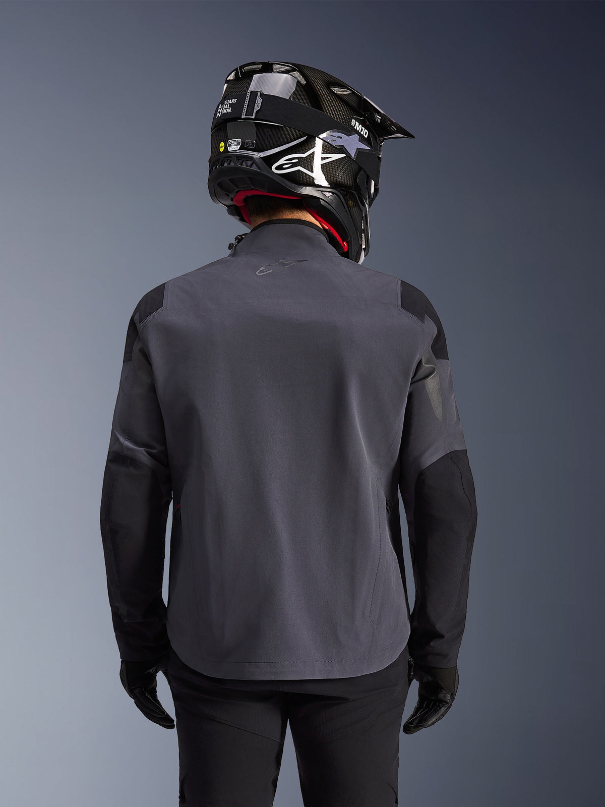 Maxdura Drystar®XF Laminated Armored Shell, Adventure Motorcycle Jacket, Deep Gray Black, rear view showing the technical textile construction and reinforced panels, worn with a black carbon fiber helmet, black riding pants, and gloves