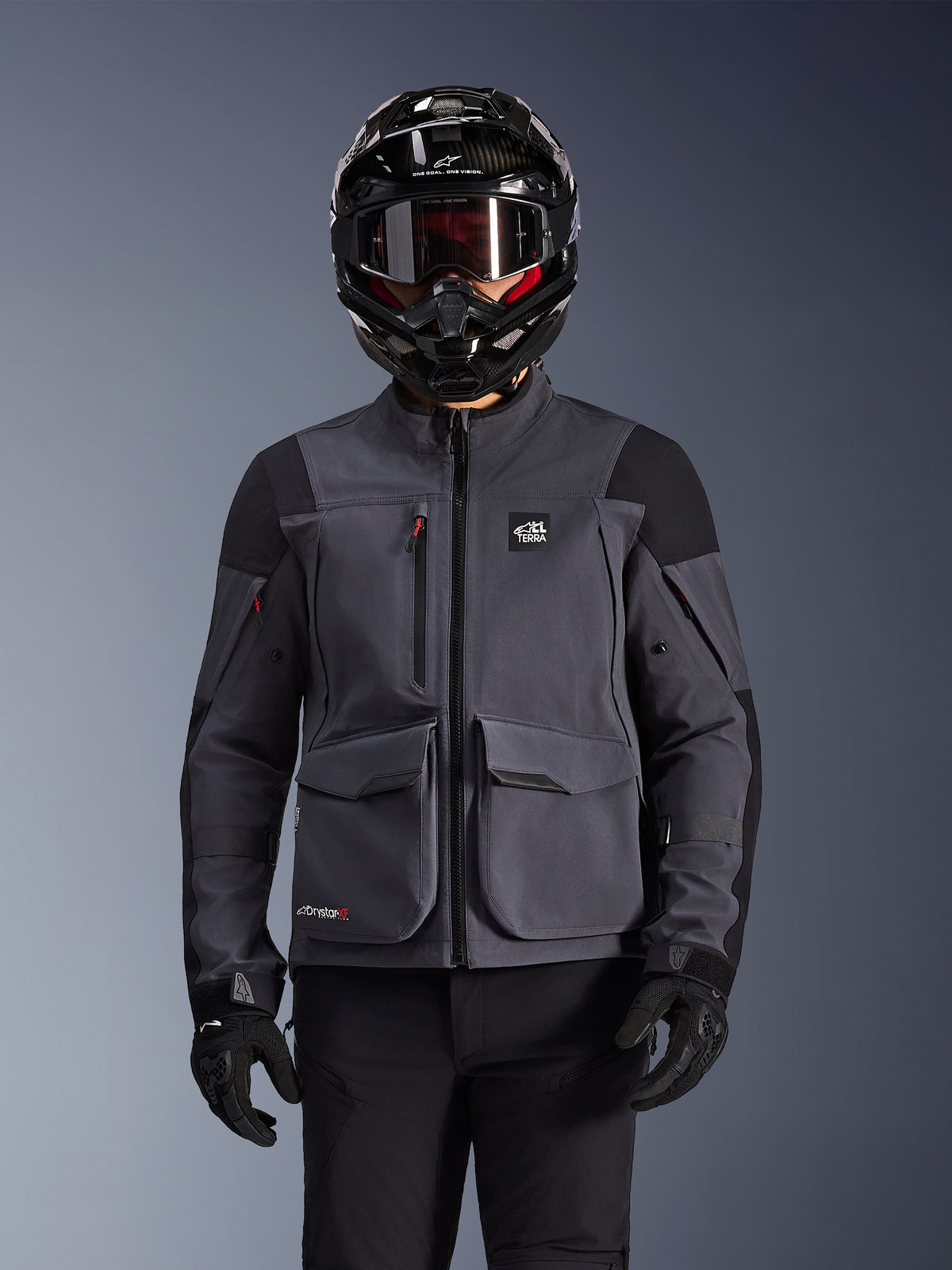 Alpinestars Maxdura Drystar®XF Laminated Armored Shell, Motorcycle Jacket, Deep Gray and Black, worn by a rider with a black helmet, goggles, and gloves, featuring large technical cargo pockets and ALL TERRA branding, adventure touring gear
