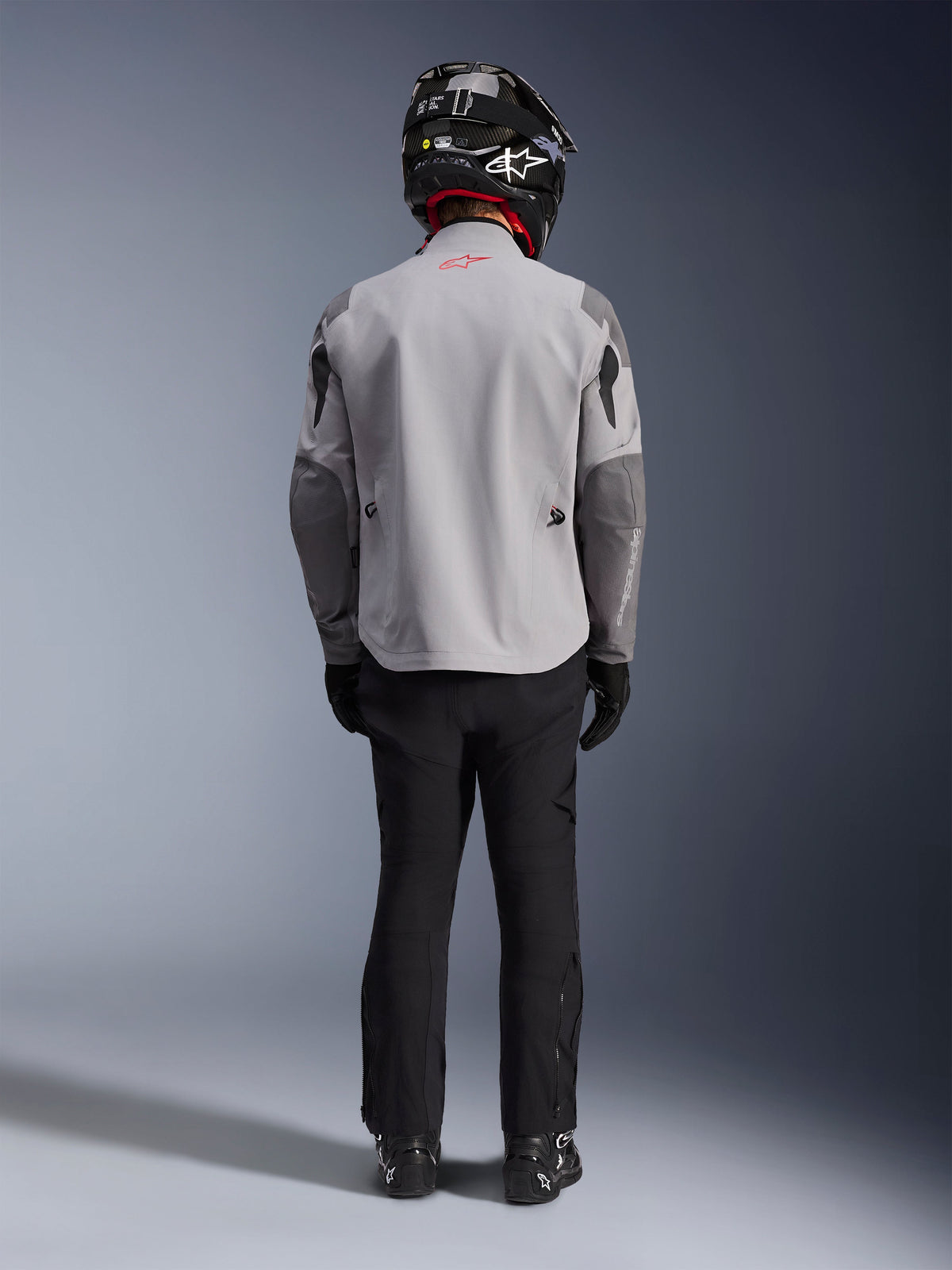 Alpinestars Maxdura Drystar®XF Laminated Armored Shell, veste de moto gris moyen et gris foncé, vue de dos sur un pilote, portée avec un pantalon noir, des bottes noires et un casque noir et blanc, équipement d'aventure touring
